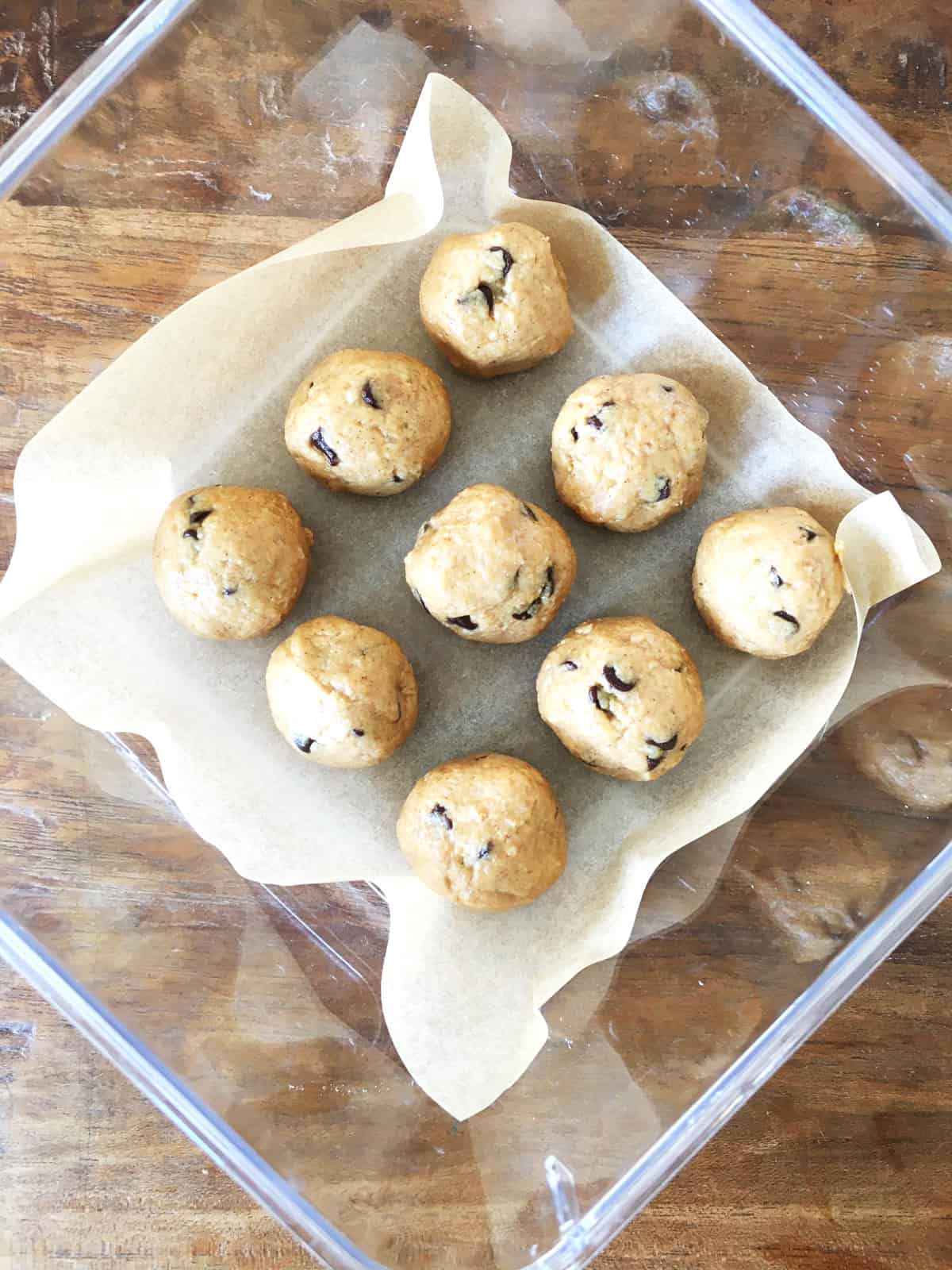 Peanut butter protein balls in a glass Tupperware container lined with parchment paper