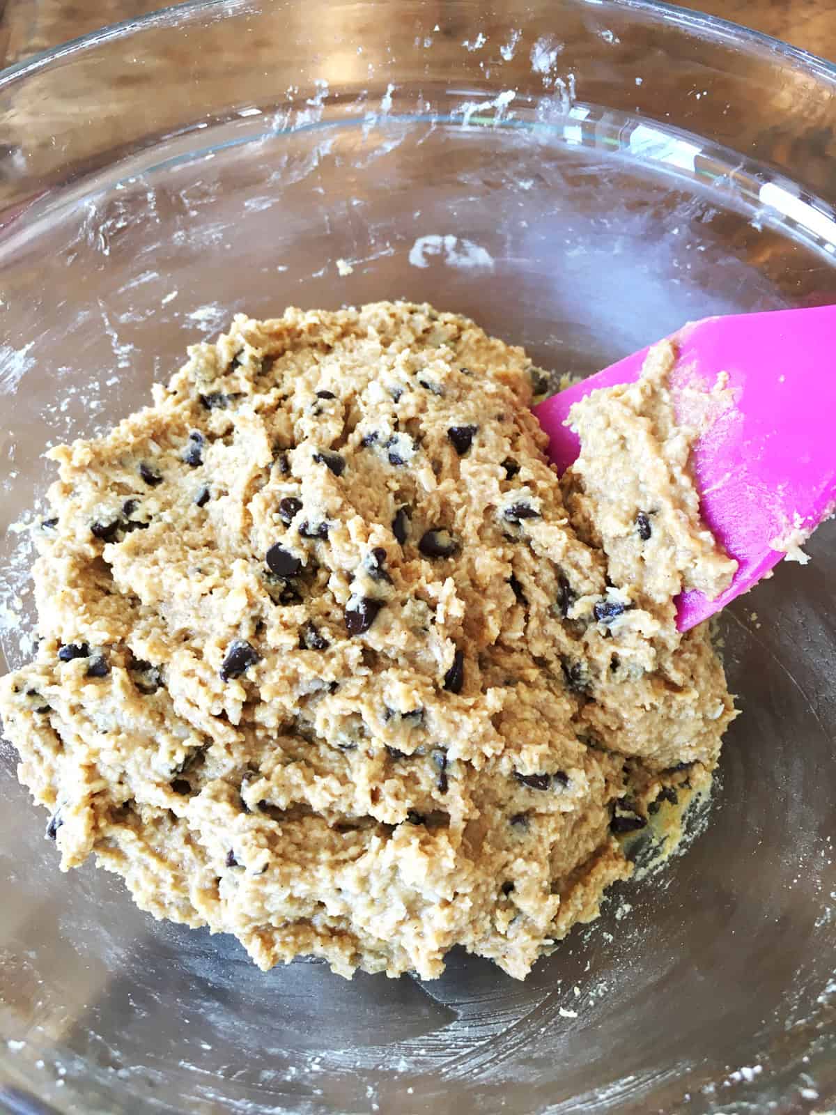 Protein ball batter with chocolate chips in a glass bowl with a purple silicone spatula