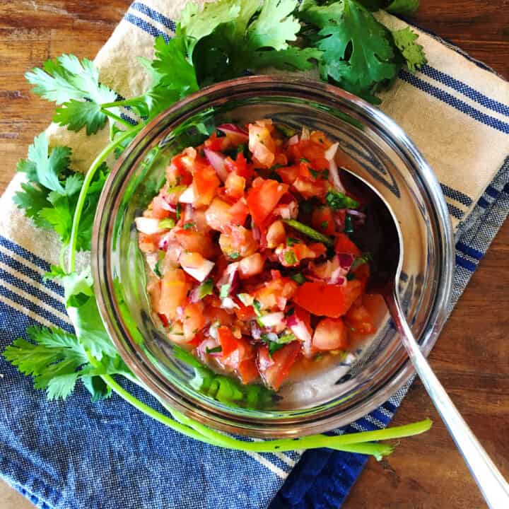 Homemade salsa in a glass bowl with a silver spoon.