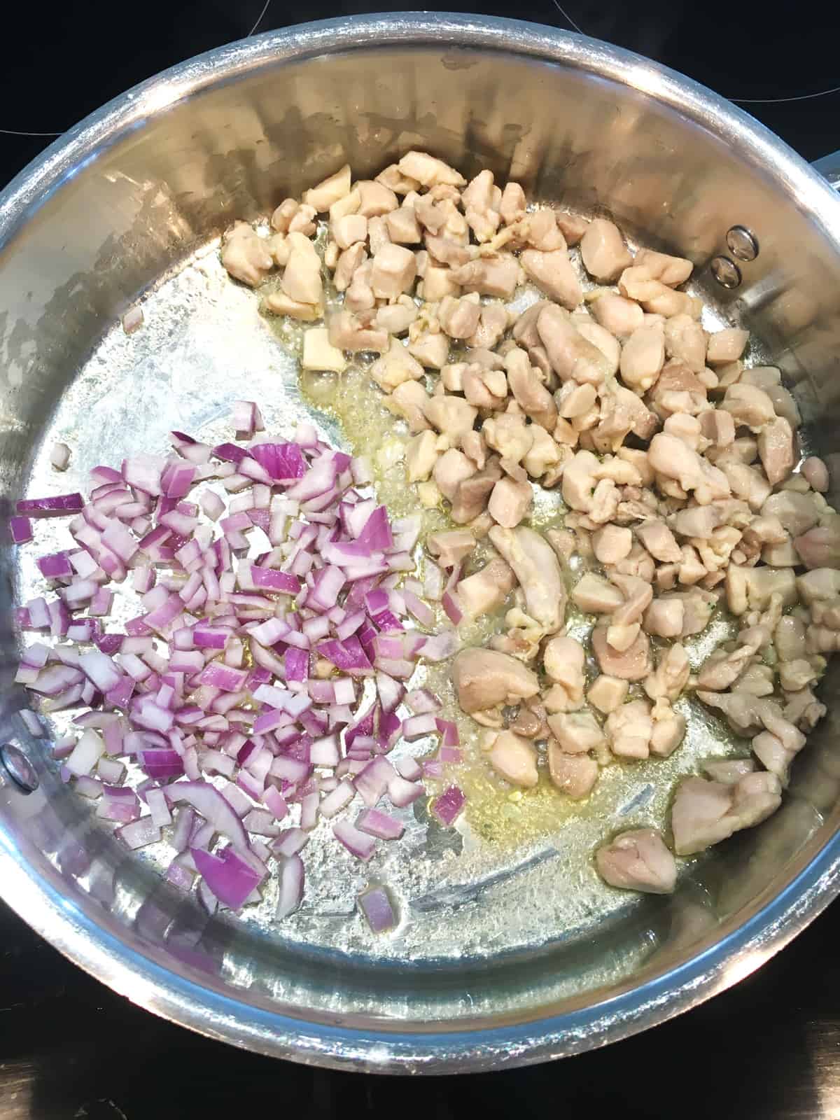 Sautéing red onions and chicken in a stainless steel pan