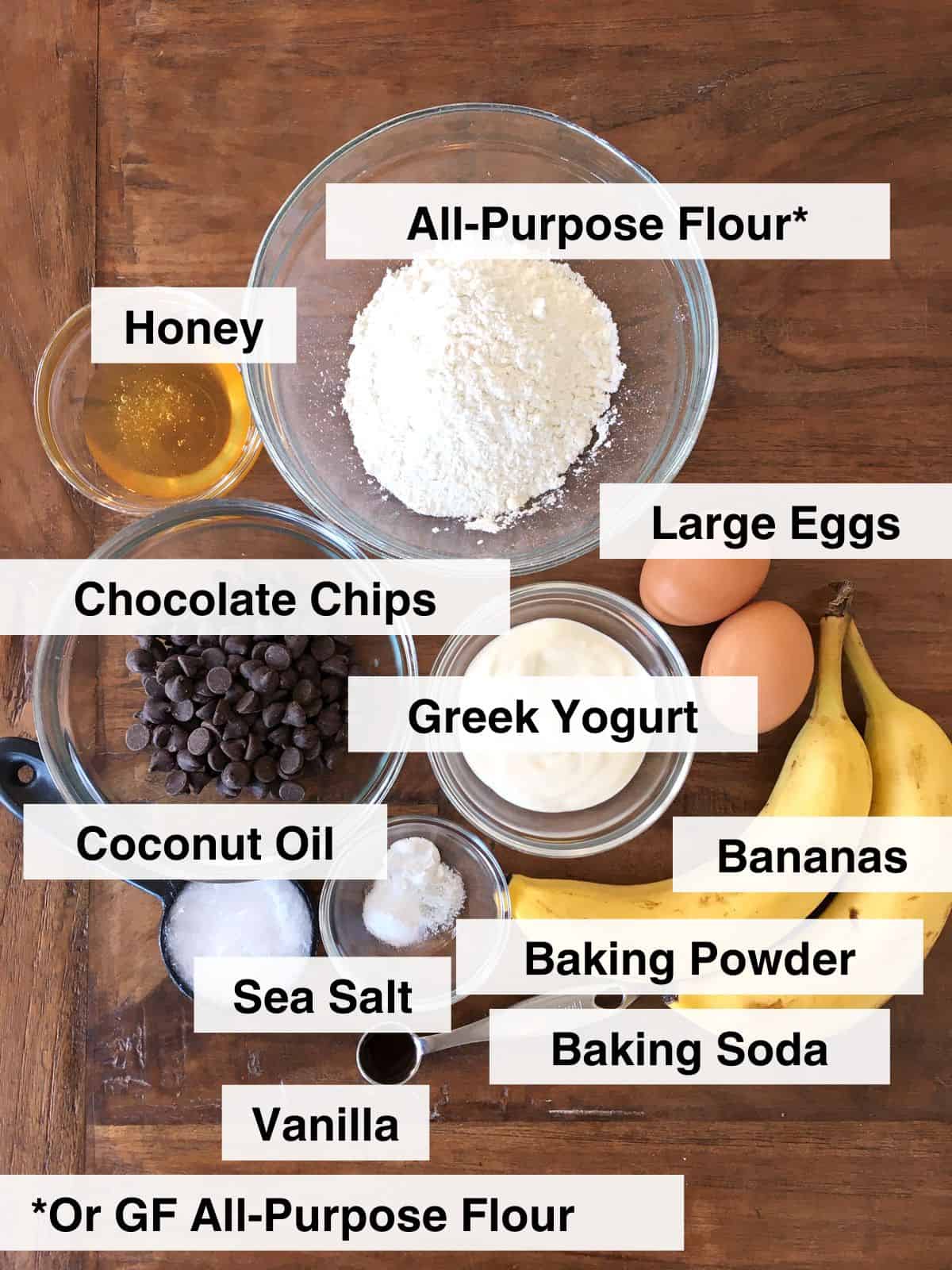 Banana chocolate chip muffin ingredients, some in glass meal prep bowls, on a brown wood table.