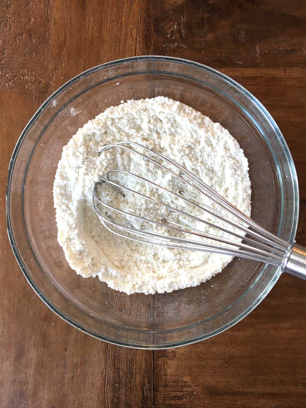 Dry ingredients for banana chocolate chip muffins in a glass bowl with a stainless steel whisk.