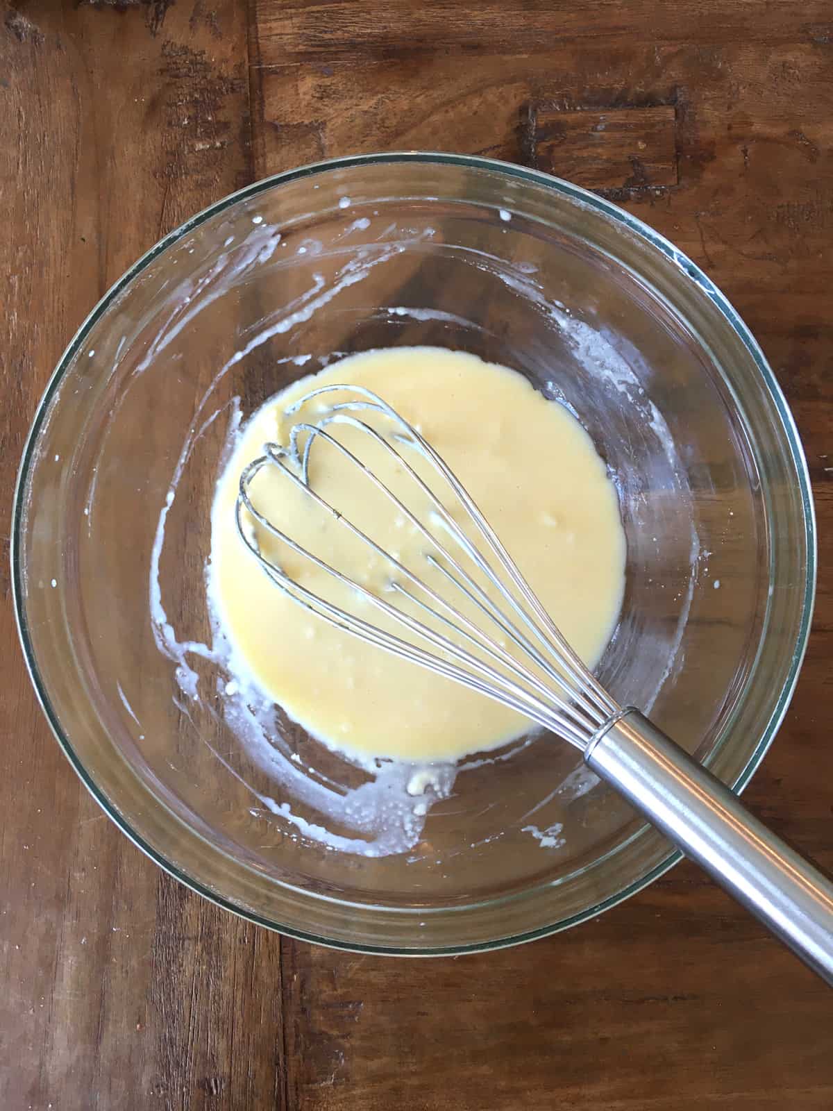 Wet ingredients for banana chocolate chip muffins in a glass bowl with a stainless steel whisk.