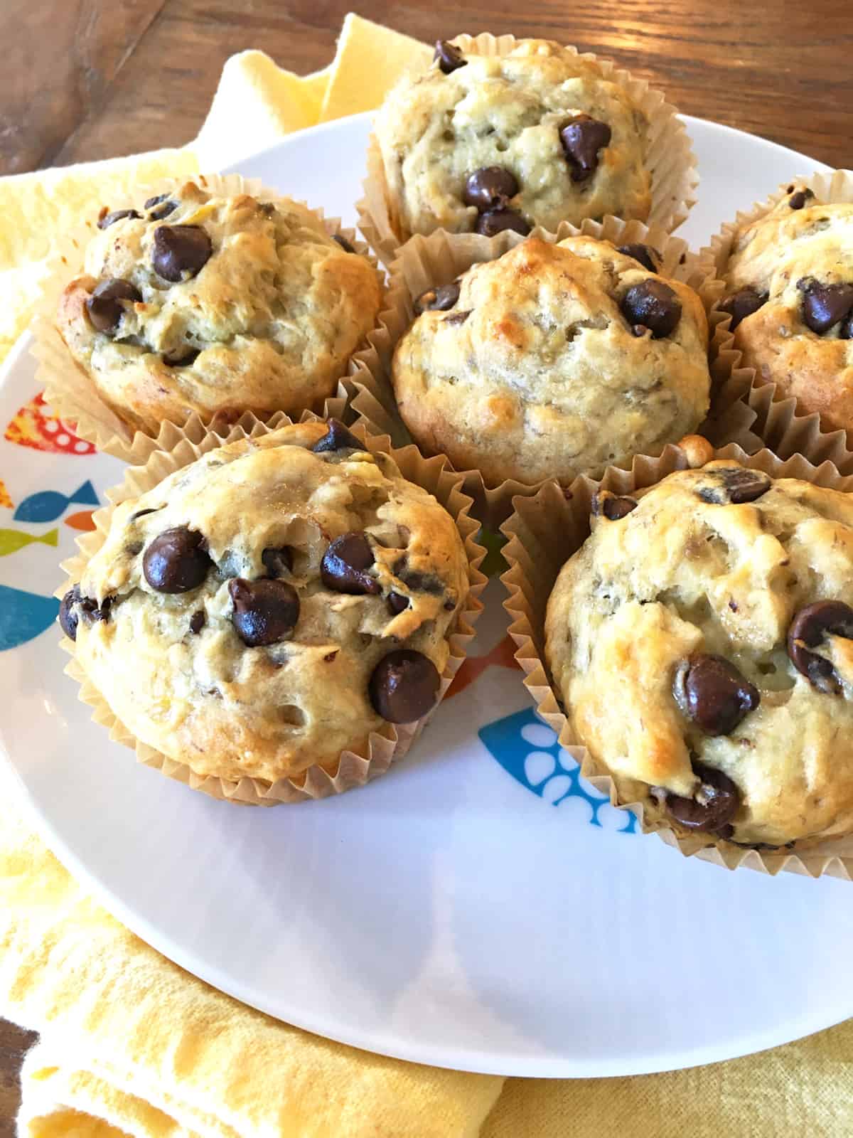 Six banana chocolate chip muffins in paper liners on a kids plate.