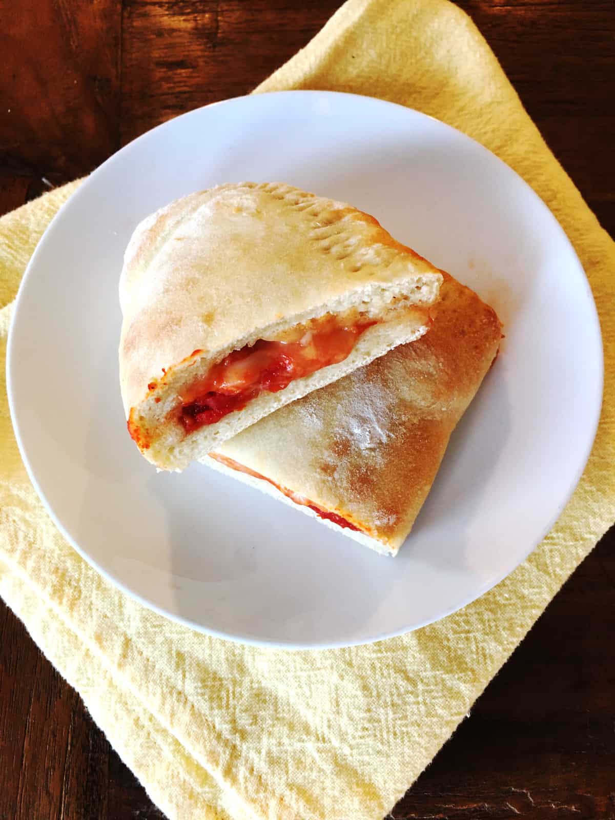 Cheese calzone sliced in half on a white plate with a yellow cloth napkin.