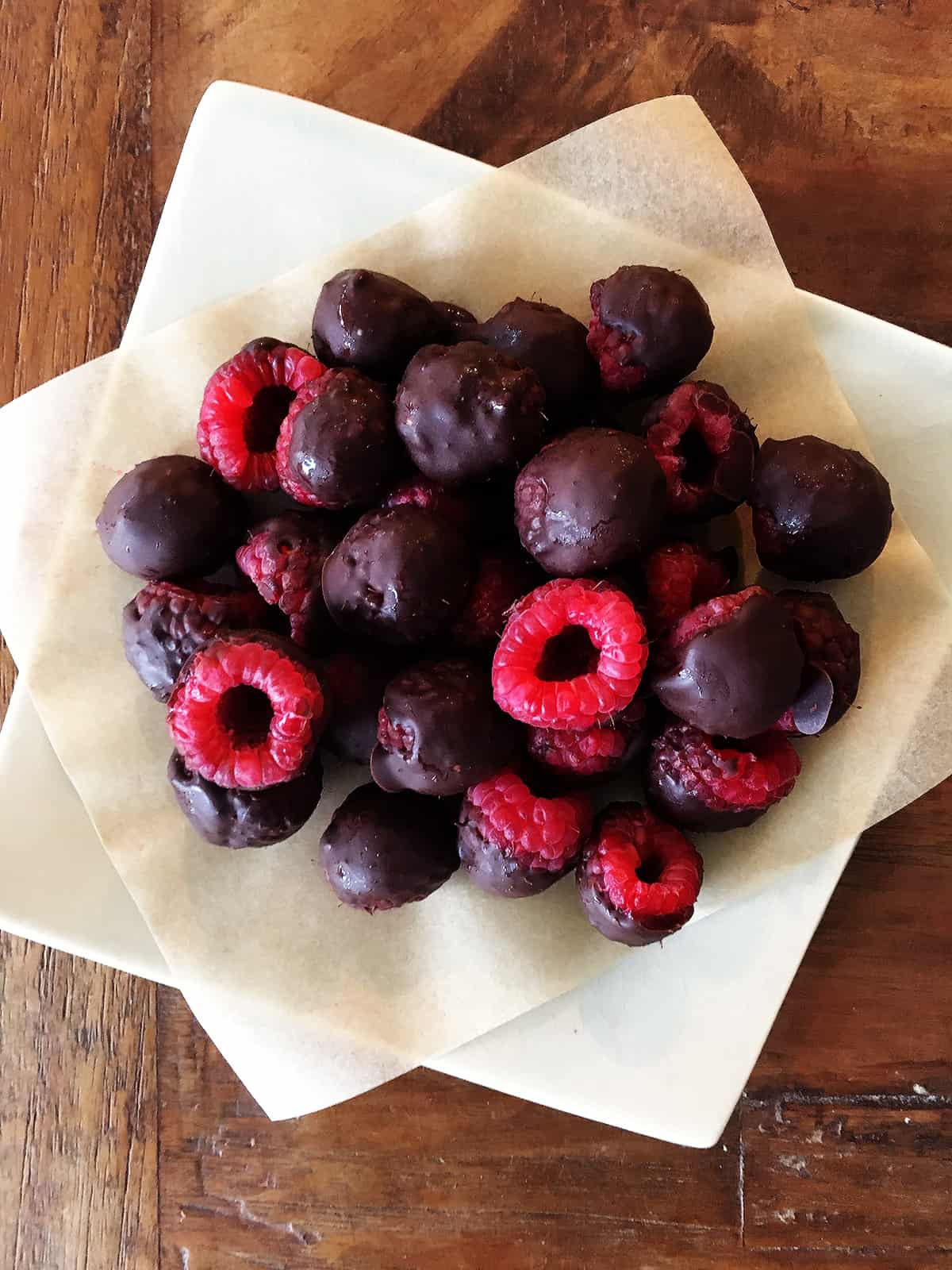 Chocolate covered raspberries on a ceramic square plate atop a brown wood table