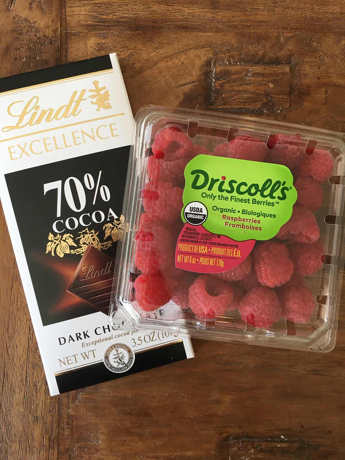 A dark chocolate bar and a container of fresh raspberries on a brown wood table