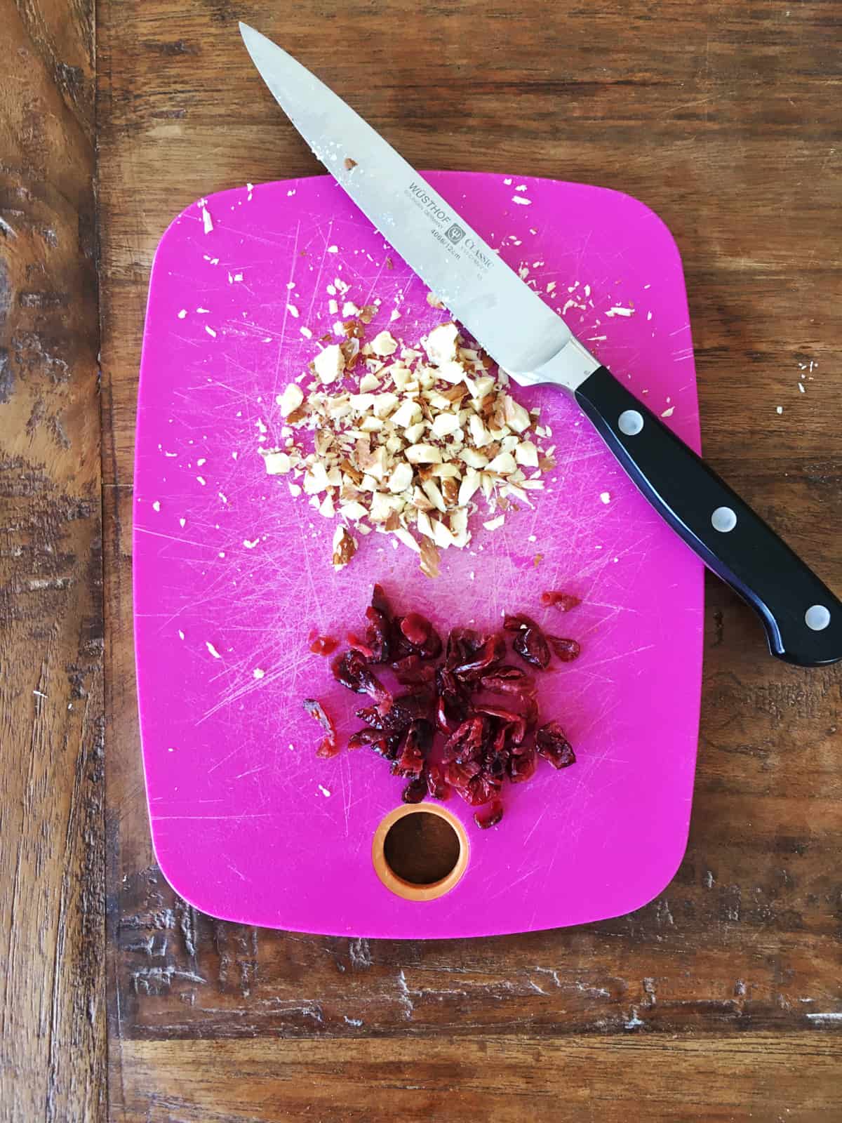 Chopped almonds and dried cranberries with a sharp knife on a purple cutting board