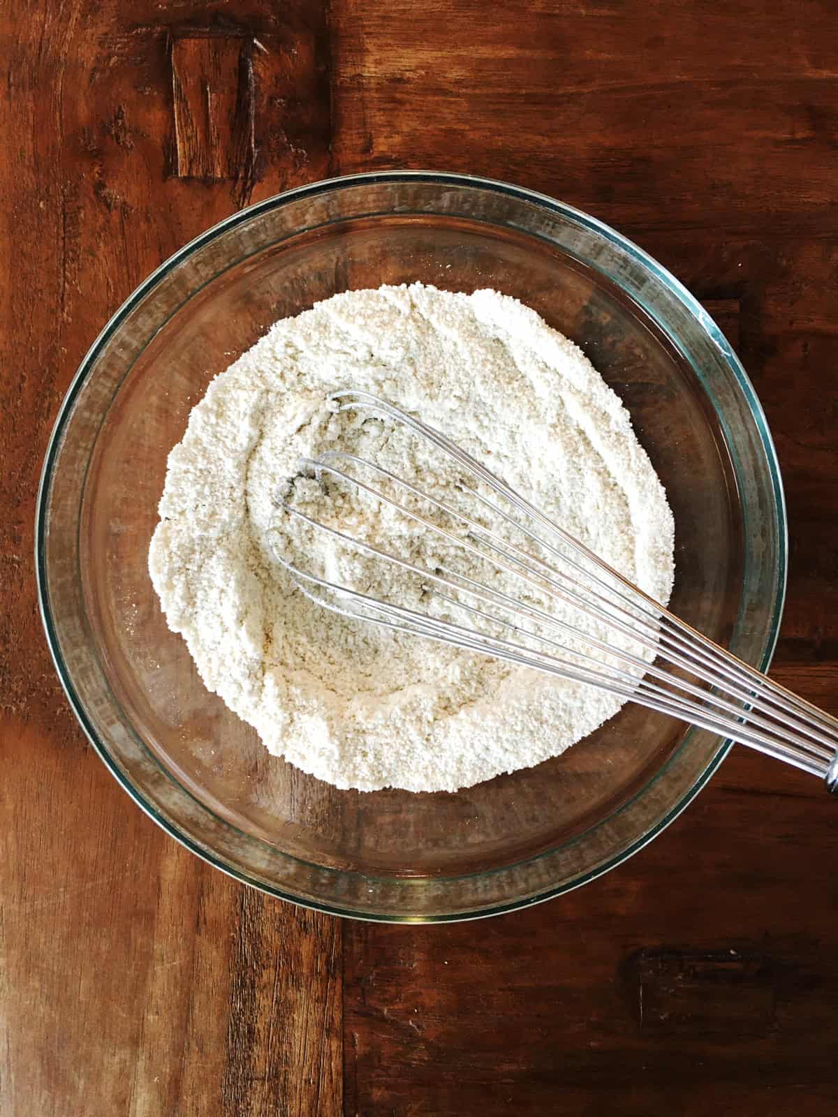 Dry ingredients for pancakes in a glass mixing bowl with a stainless steel whisk