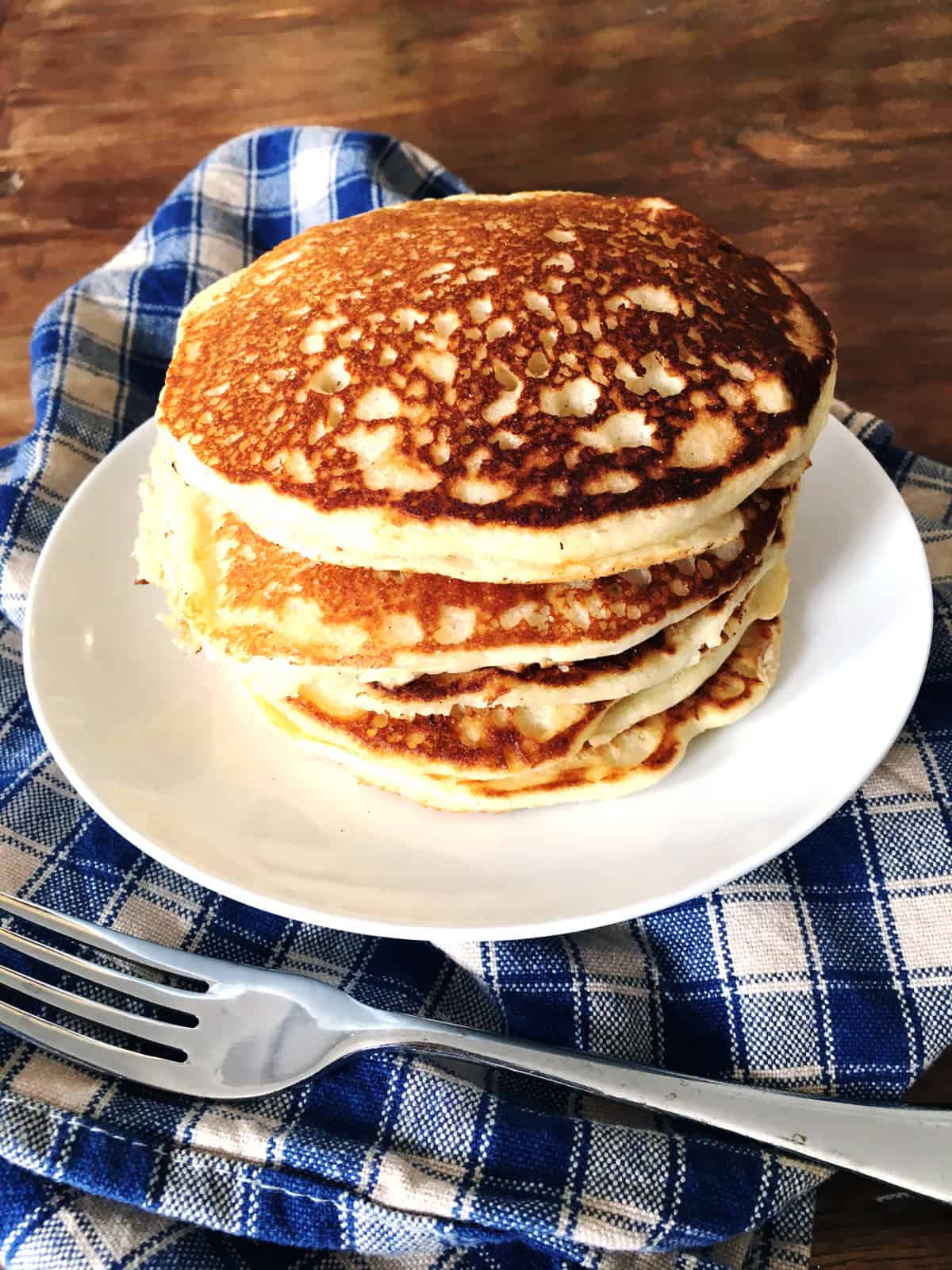 Stack of gluten free pancakes on a white plate with a blue and tan plaid napkin.