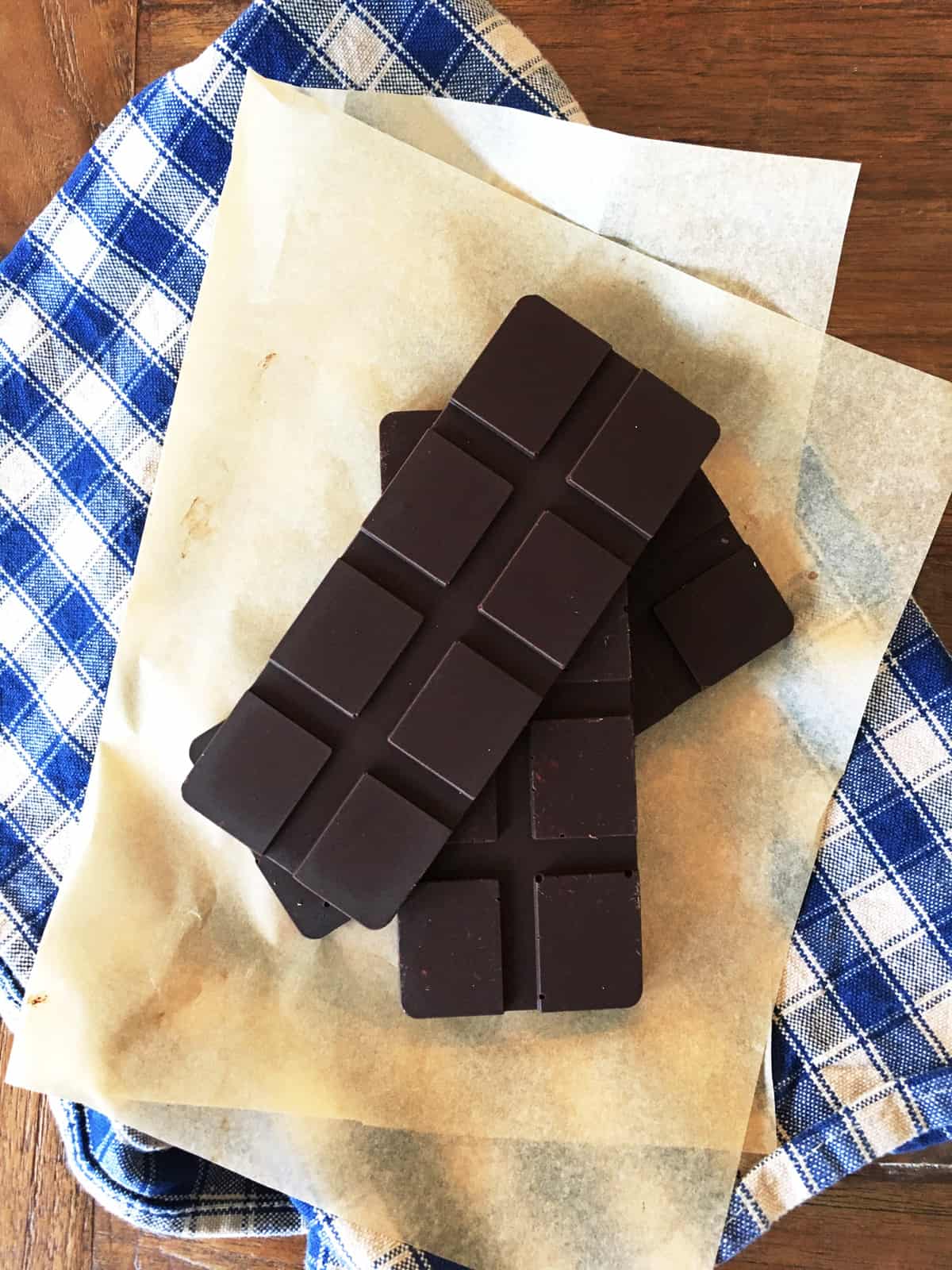 Three bars of homemade dark chocolate on parchment paper with a blue and tan checkered napkin.