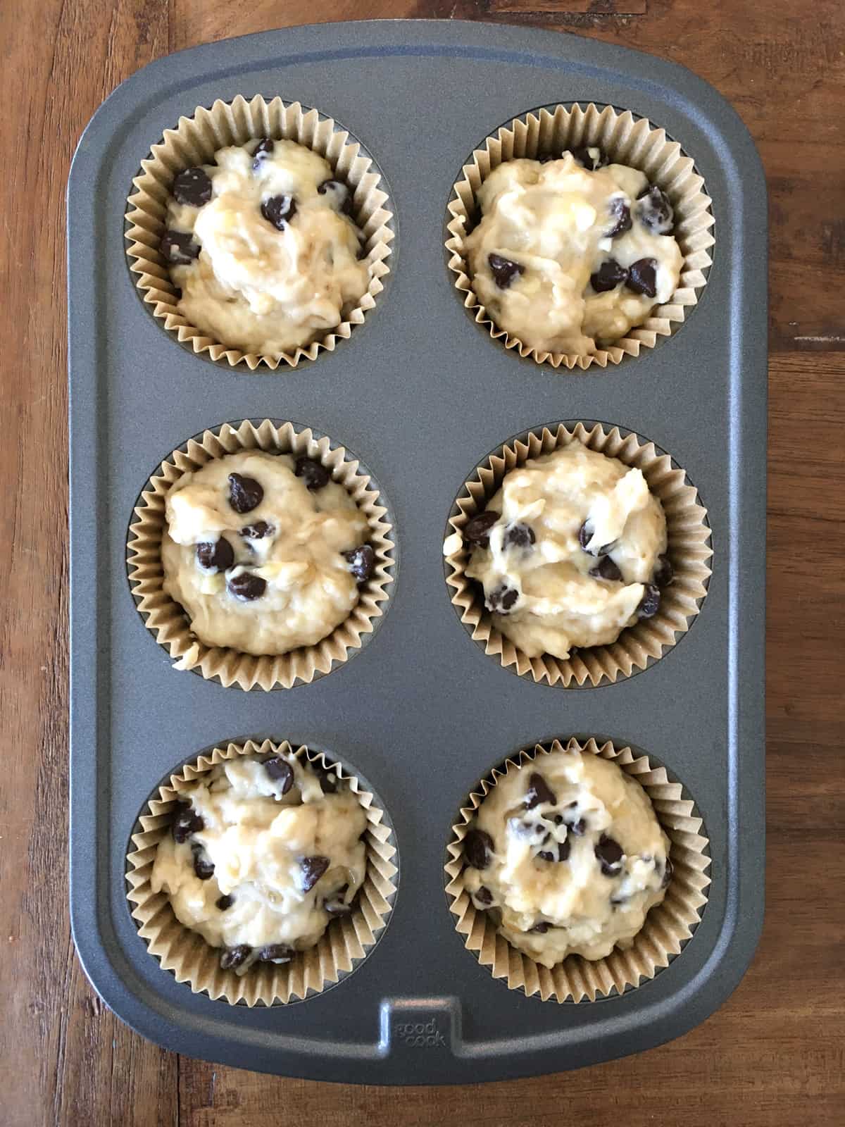 Six-muffin tin lined and filled with banana chocolate chip muffin batter.