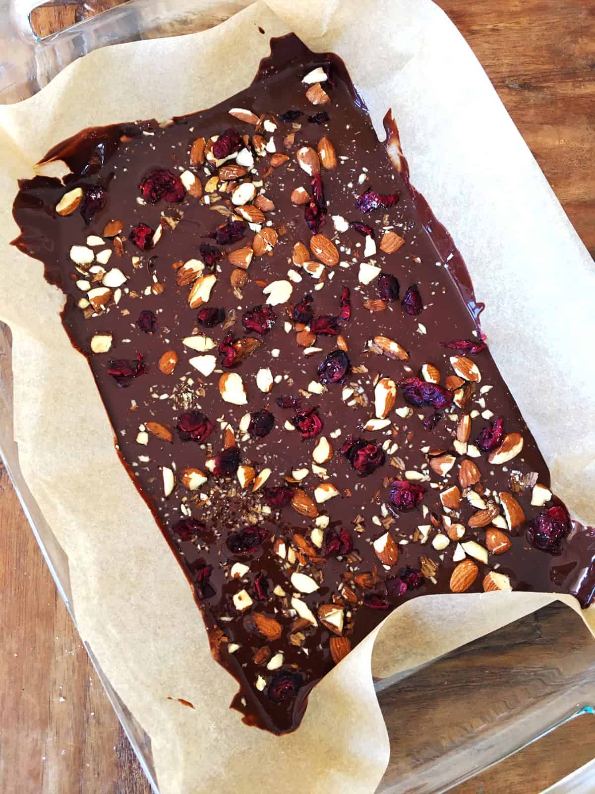 Chocolate bark with almonds and cranberries in a lined baking dish.