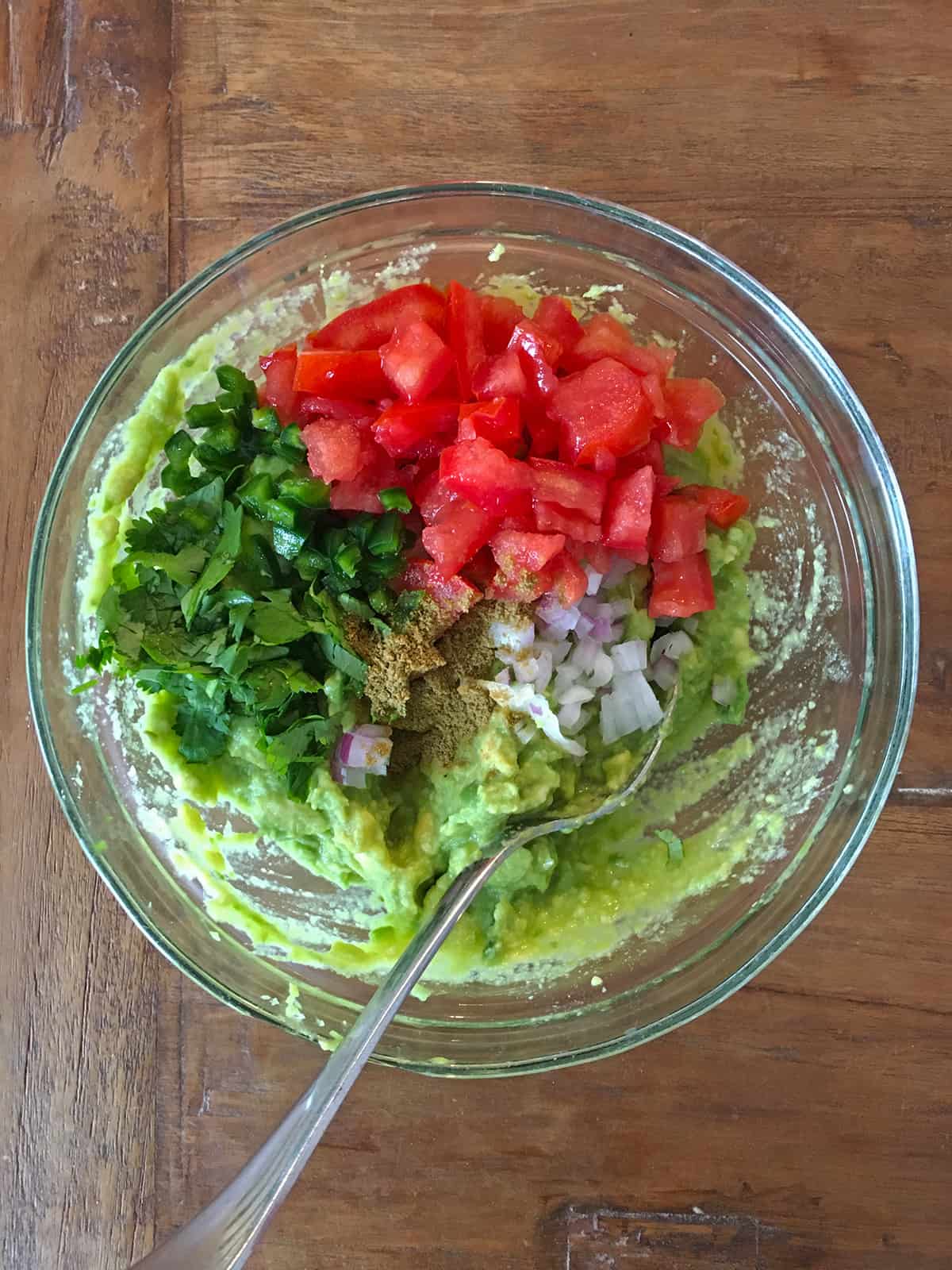 Guacamole ingredients in a glass mixing bowl with a spoon