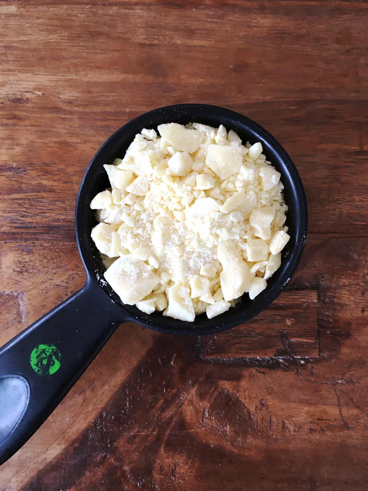 Cocoa butter chunks in a black plastic measuring cup on a brown wood table.