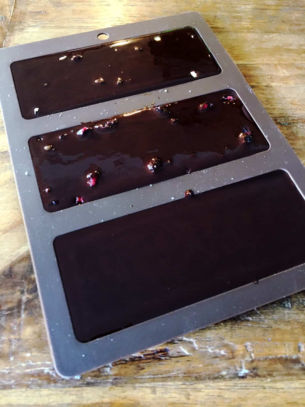 Freshly made chocolate poured into a chocolate bar mold on a brown wood table.