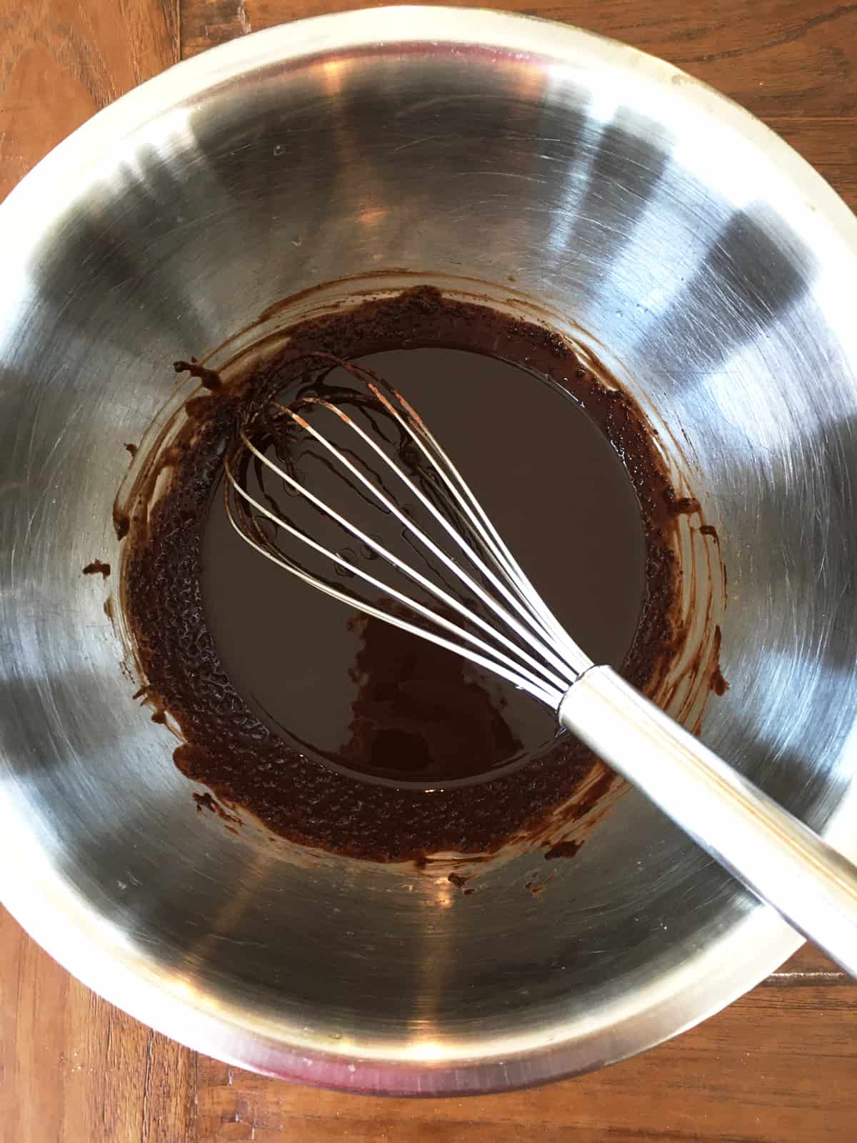 Freshly made melted dark chocolate in a stainless steel mixing bowl with a whisk.