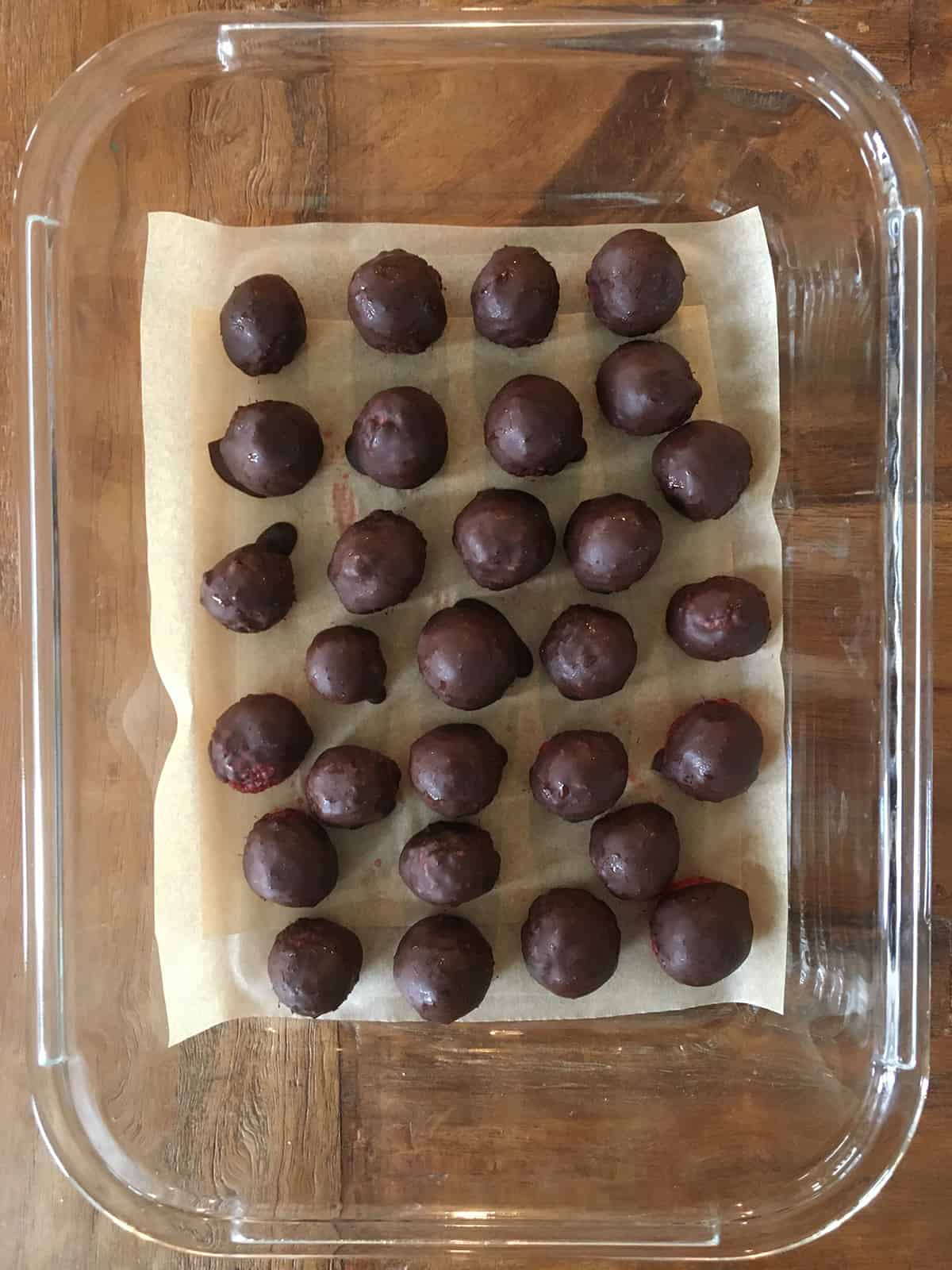 Chocolate covered raspberries in a parchment paper lined glass dish
