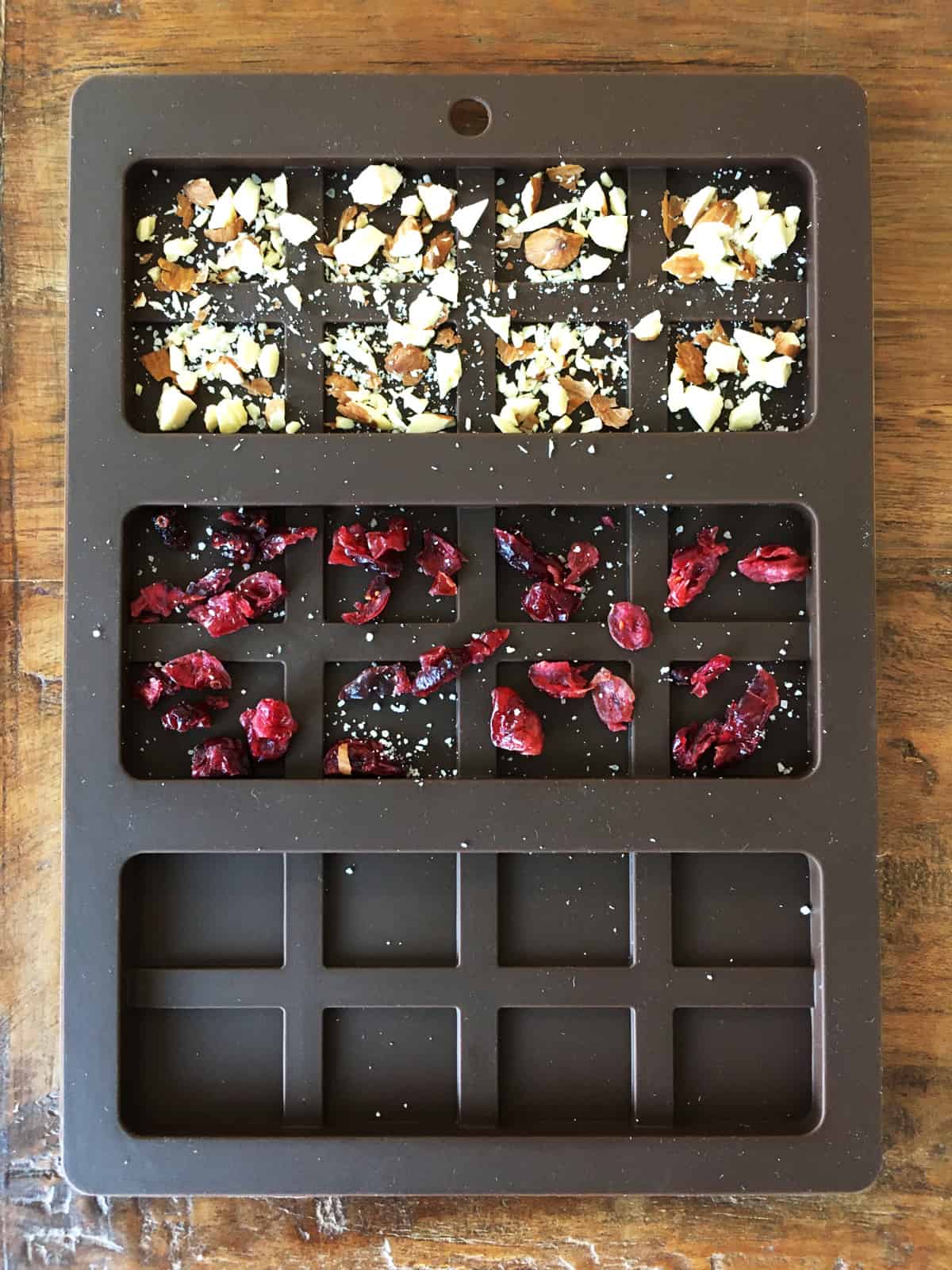 Chocolate bar mold partially filled with chopped almonds, dried cranberries and sea salt.