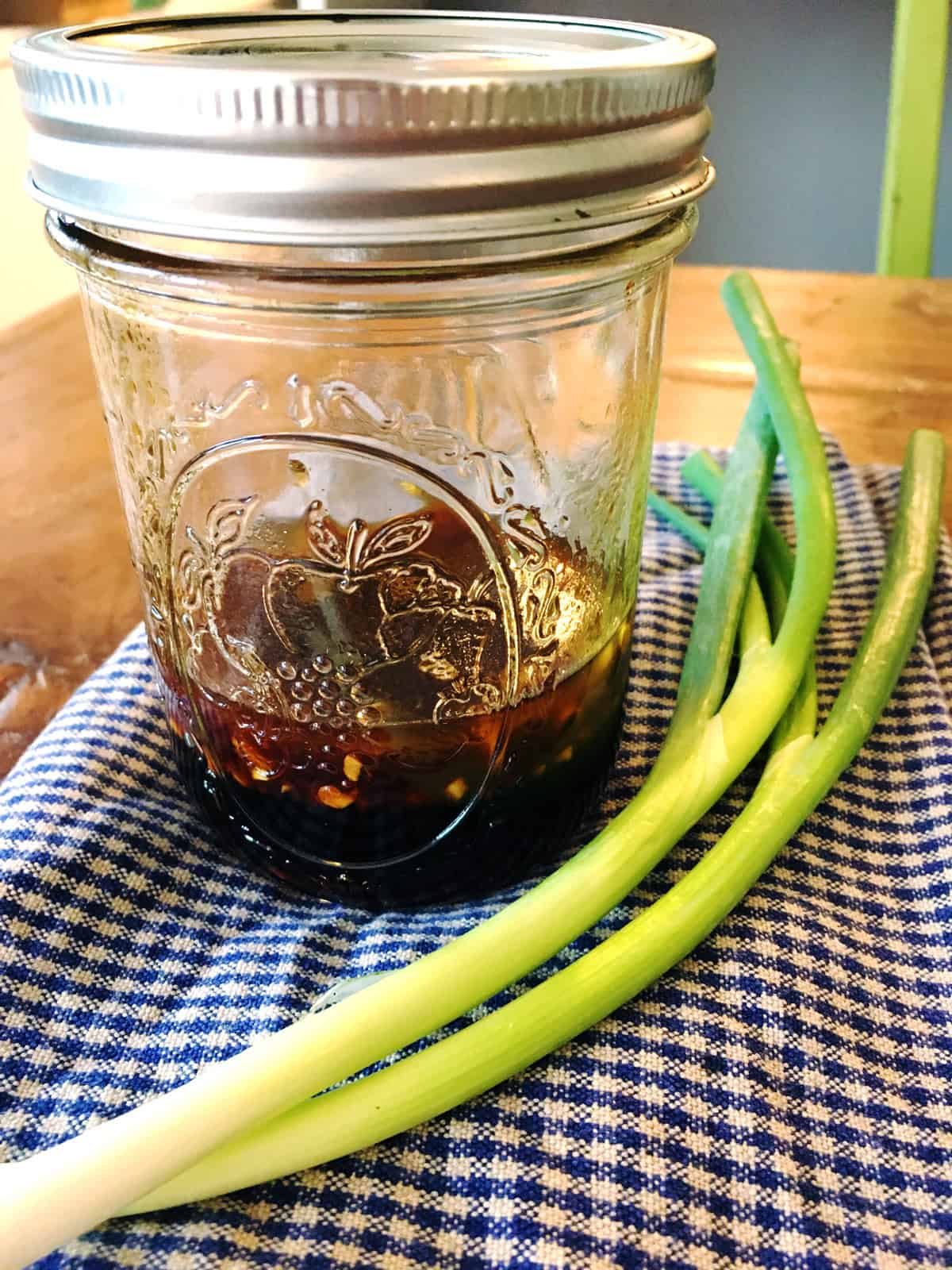 Asian salad dressing in a small Mason jar on a blue and tan checkered napkin.