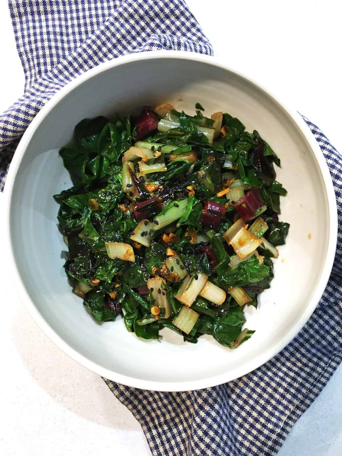 Asian sautéed Swiss chard in a tan ceramic bowl with a blue and tan checkered napkin