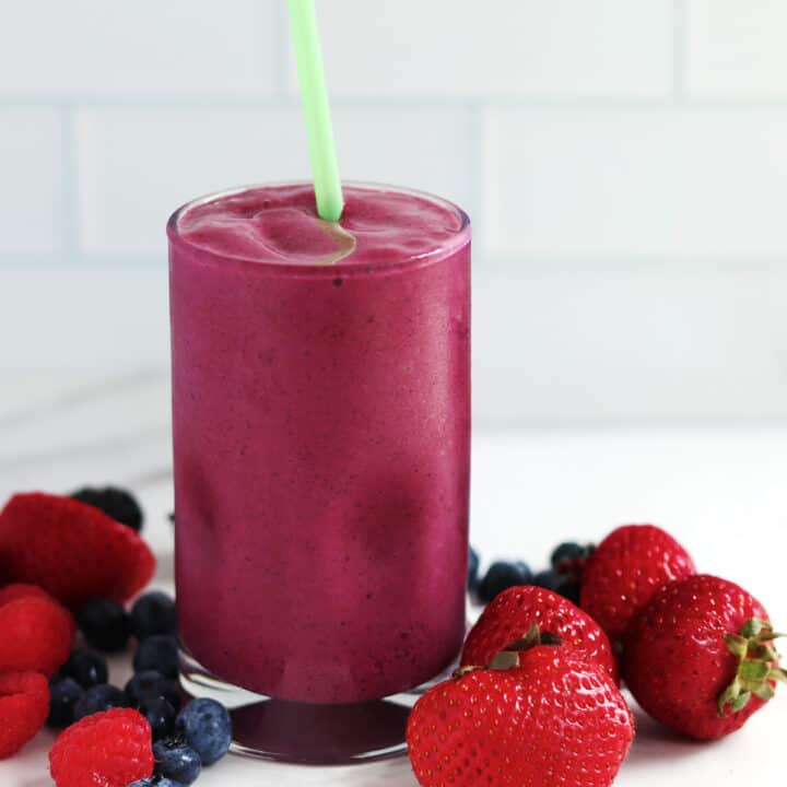 A mixed berry smoothie alongside fresh mixed berries.