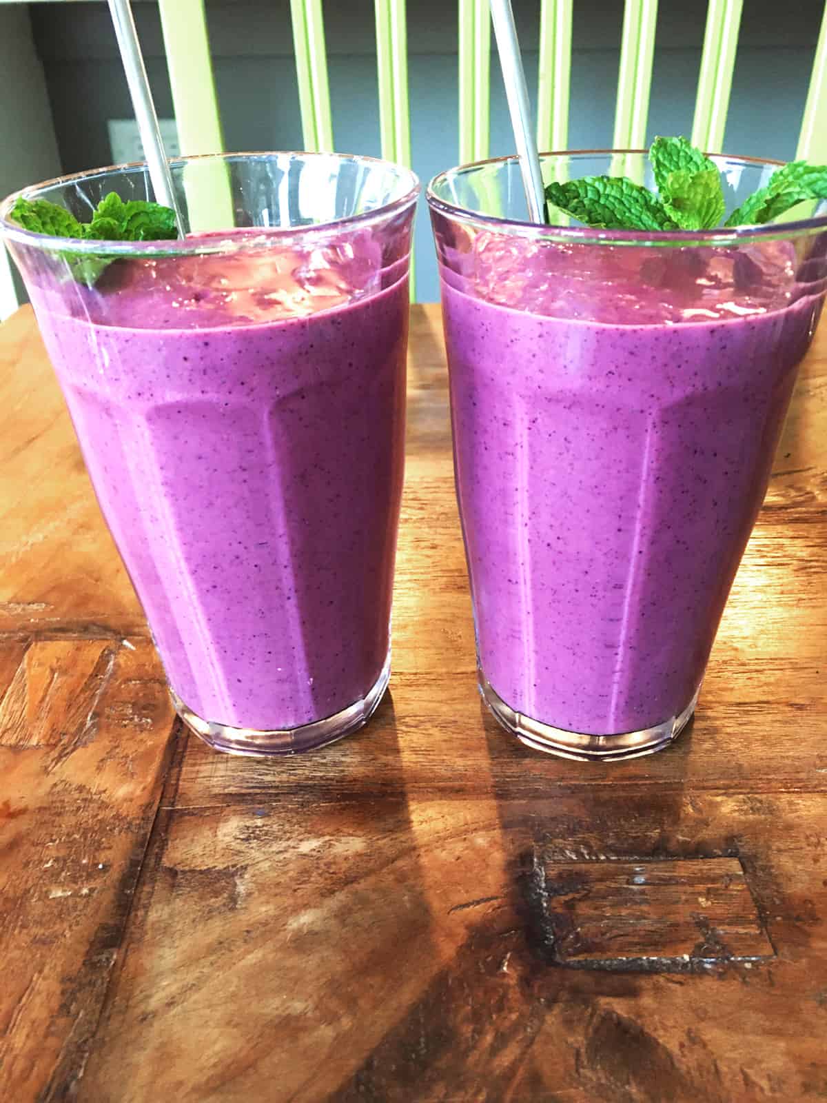 Two berry smoothies garnished with fresh mint on a brown wood table.