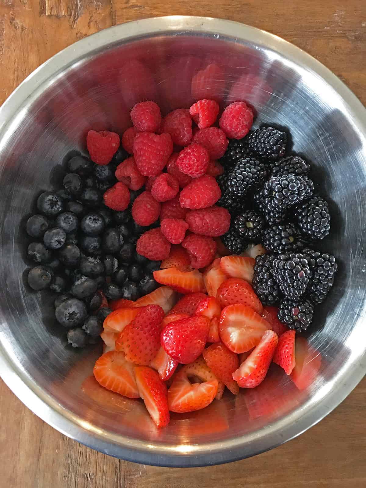 Fresh blueberries, raspberries, blackberries and strawberries in a stainless steel mixing bowl