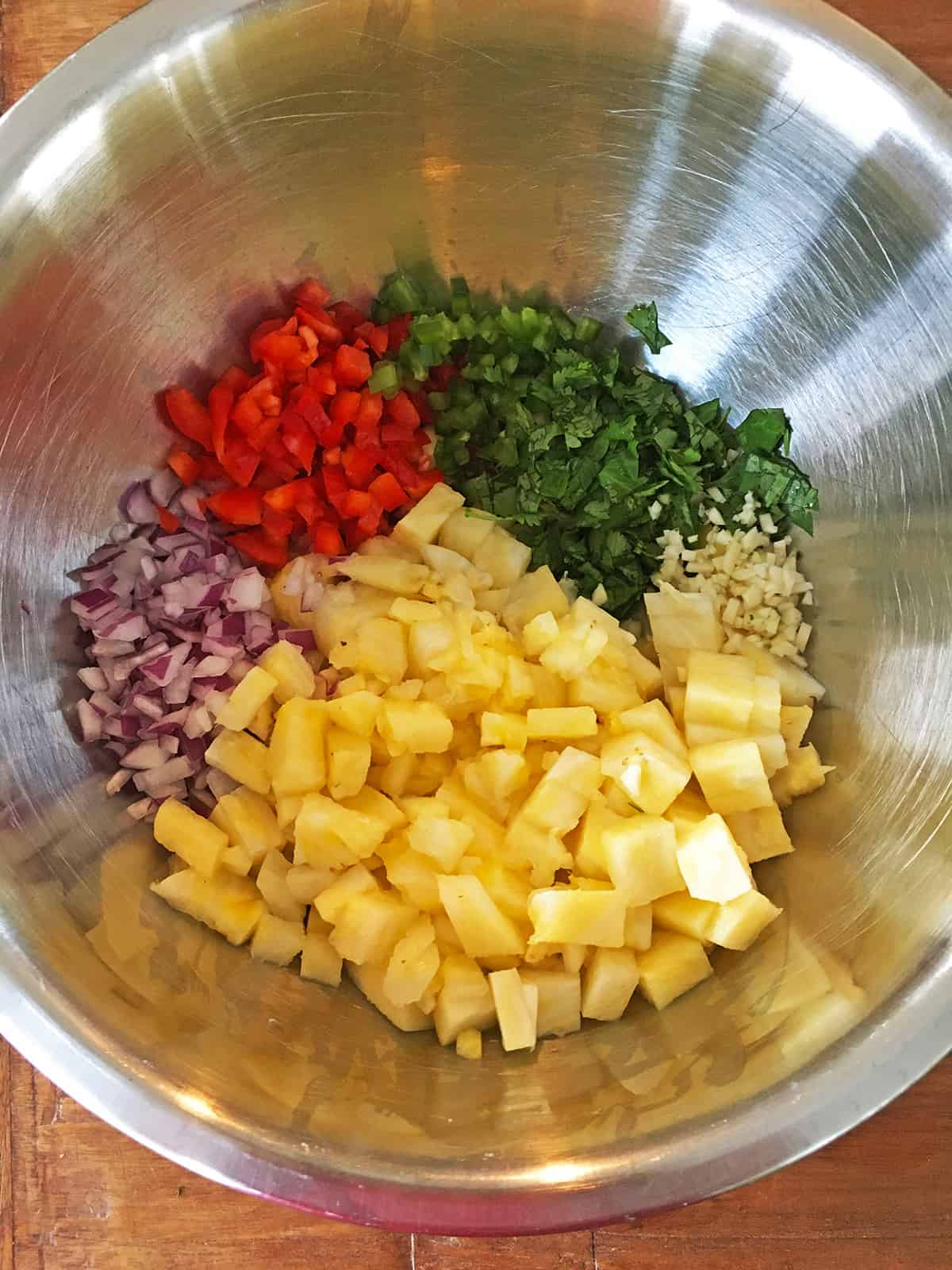 Chopped pineapple salsa ingredients in a stainless steel mixing bowl