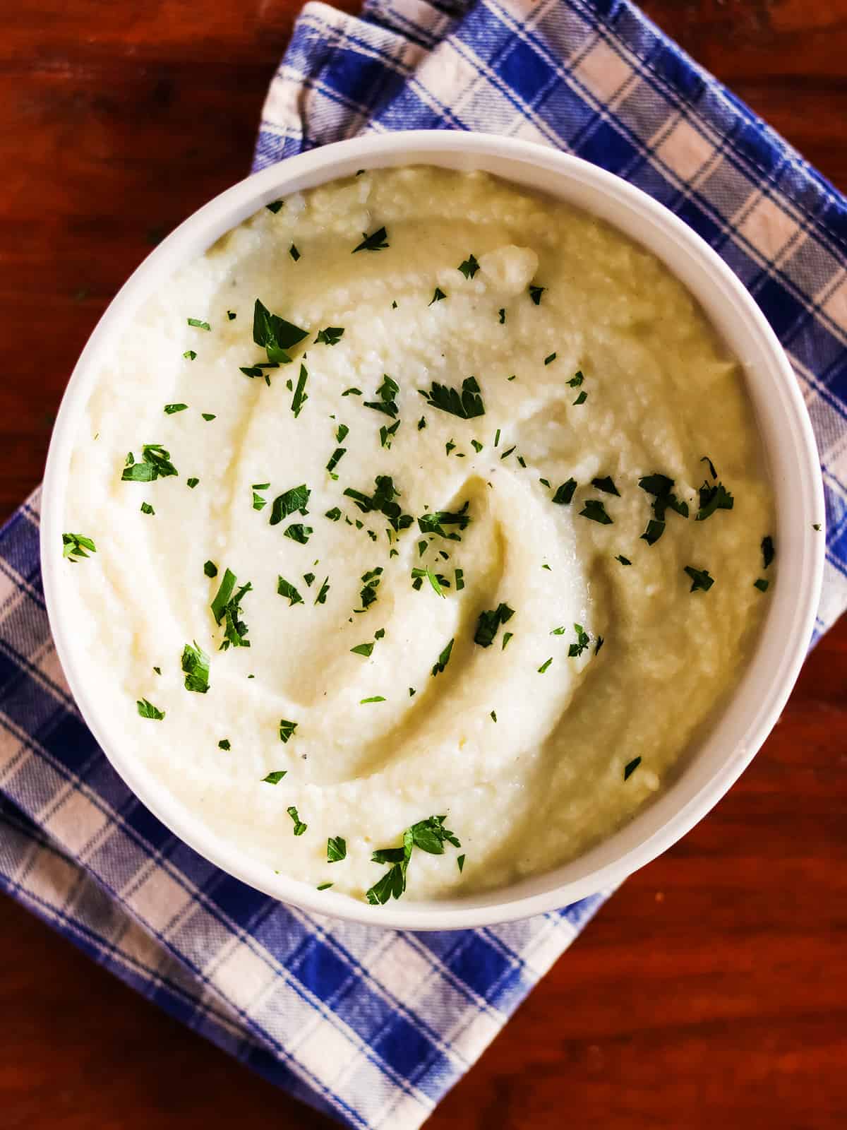 Garlic mashed cauliflower garnished with fresh parsley in a glass serving bowl.