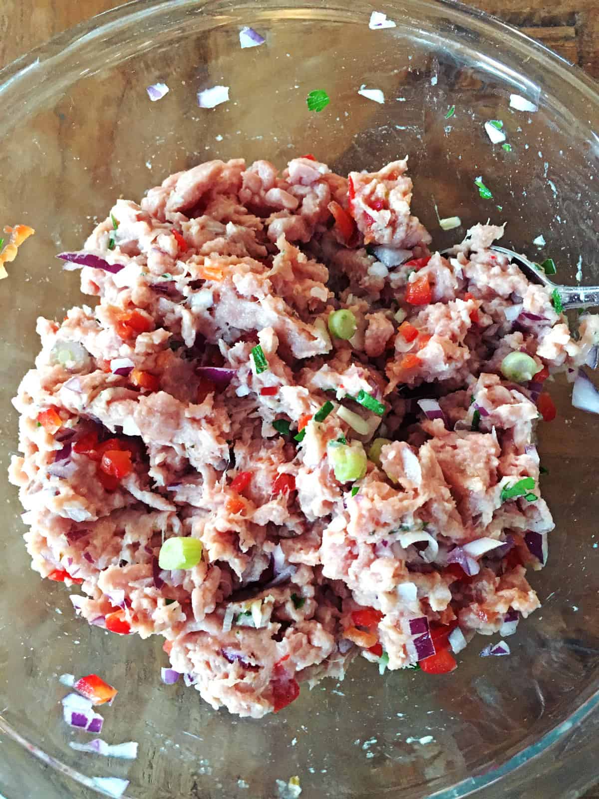 Raw turkey burger mixture in a glass mixing bowl on a brown wood table.