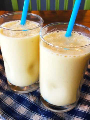 Two peach smoothies with blue straws.