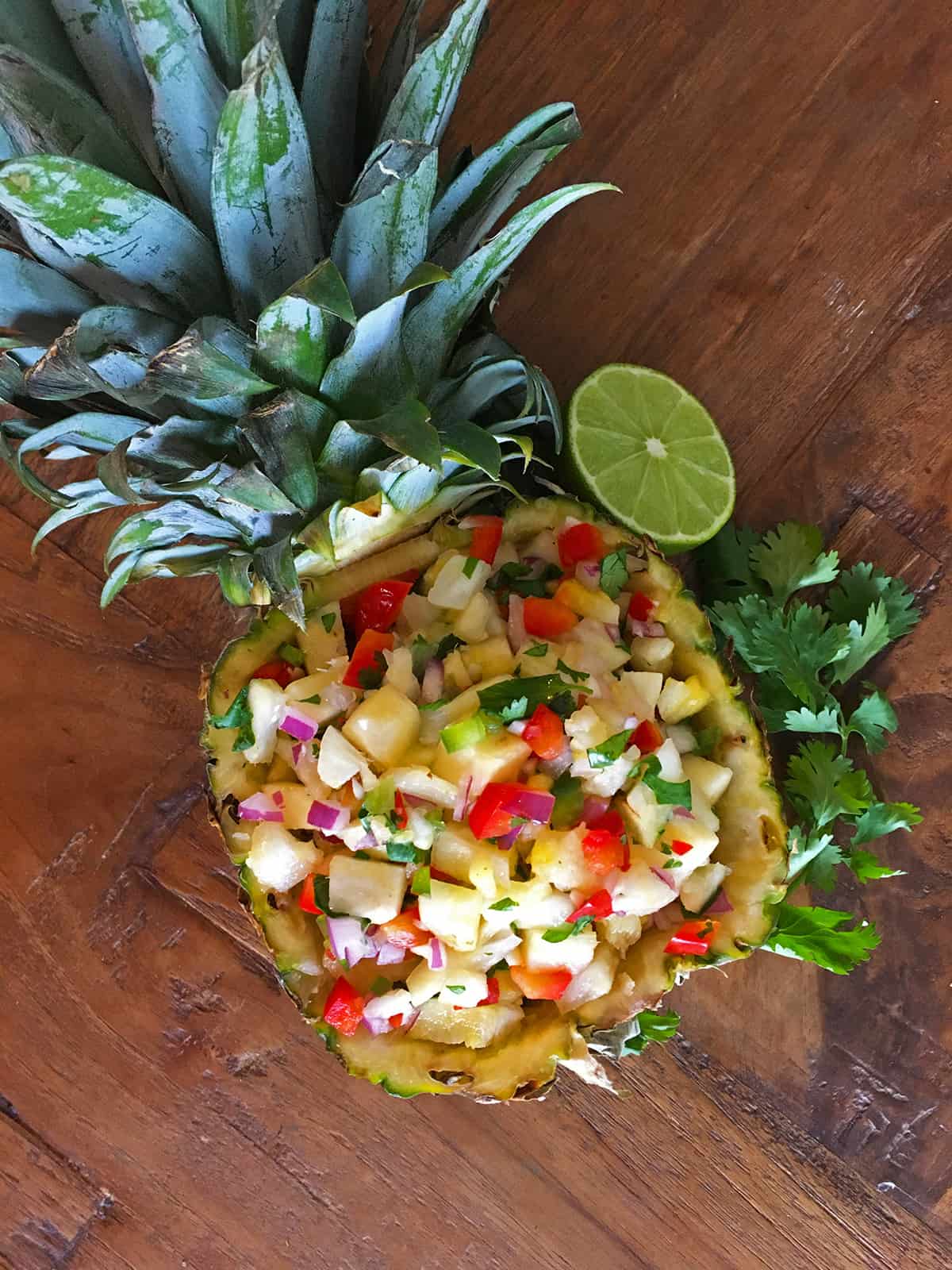 Fresh pineapple salsa in a pineapple bowl on a brown wood table
