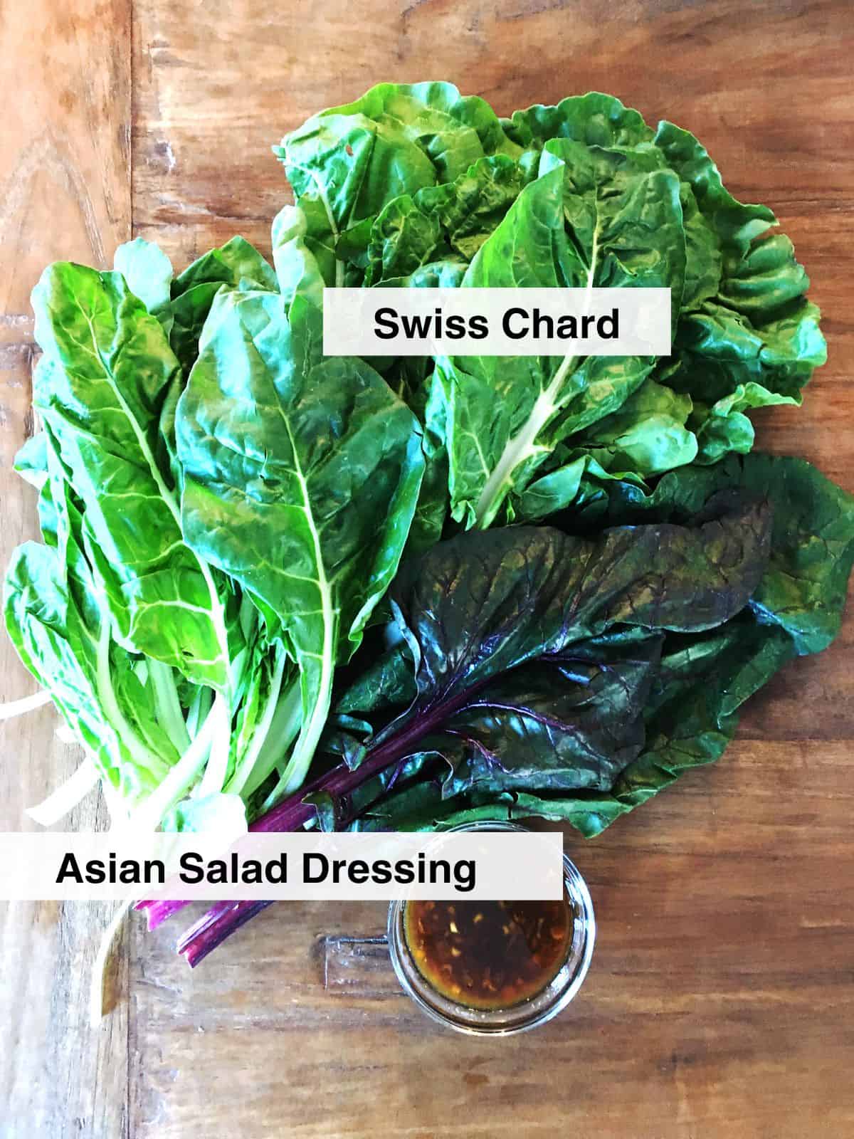 Green and red Swiss chard with a small bowl of Asian dressing on a brown wood table.