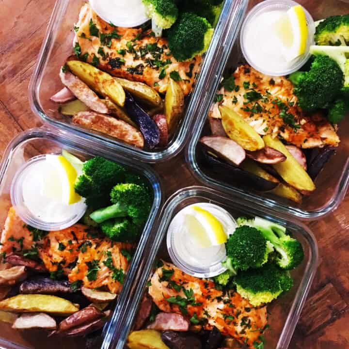 Pan seared salmon with broccoli, fingerling potatoes and garlic aioli with a slice of lemon in glass food prep containers.
