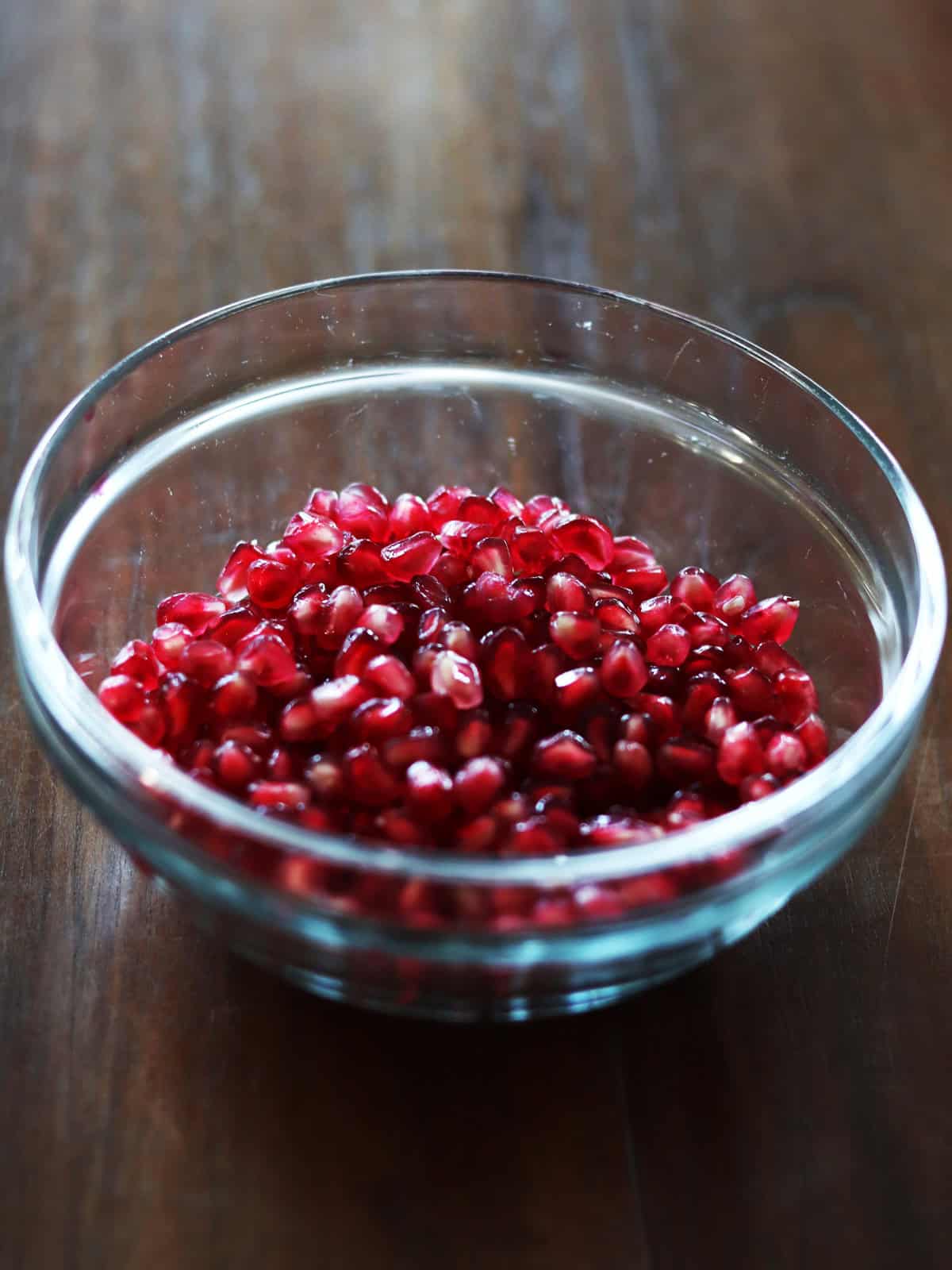 Pomegranate arils in a glass bowl on a brown wood table.