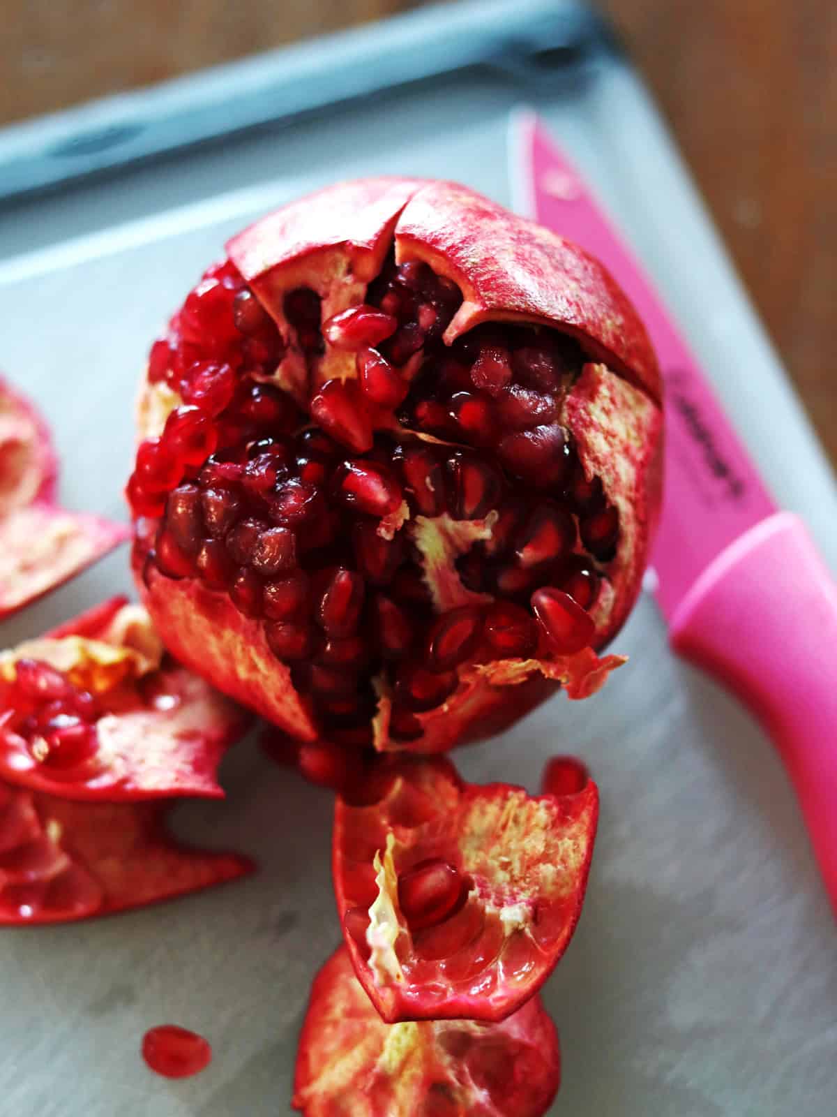 Partially peeled pomegranate on a silicone cutting board.