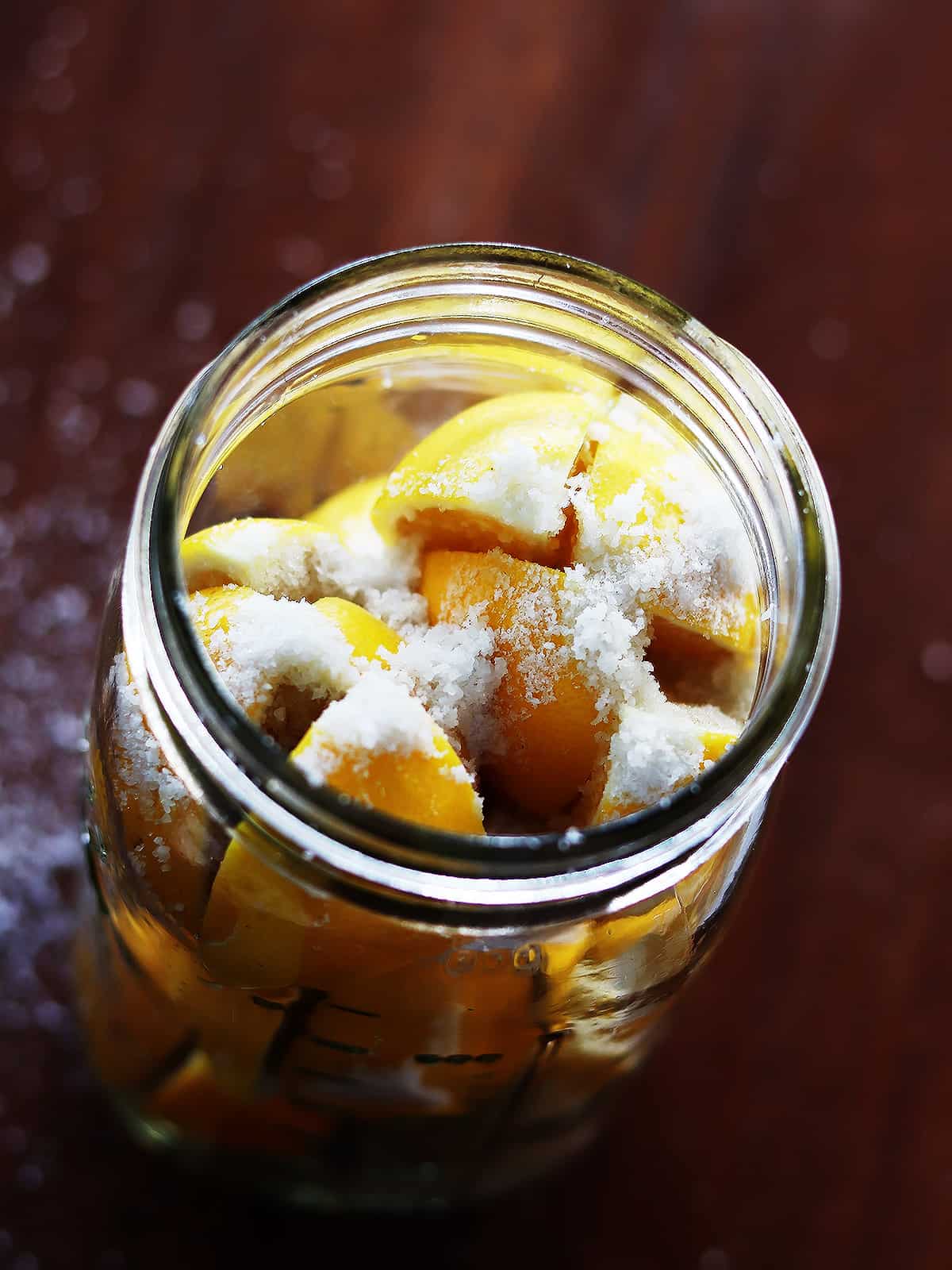 Salted lemon sections in a tall Mason jar on a brown wood table.