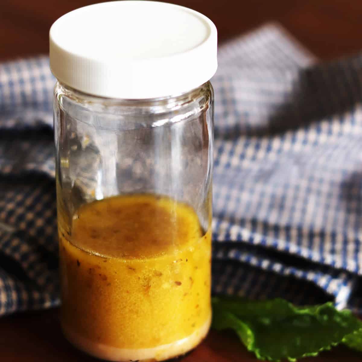 Thin glass bottle of Greek salad dressing with a blue and tan plaid napkin.