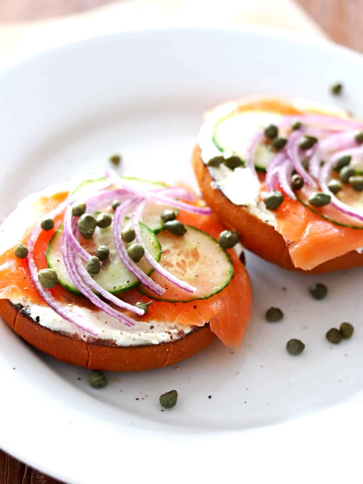 Open-faced lox and bagel sandwich topped with sliced red onion, cucumber and capers.