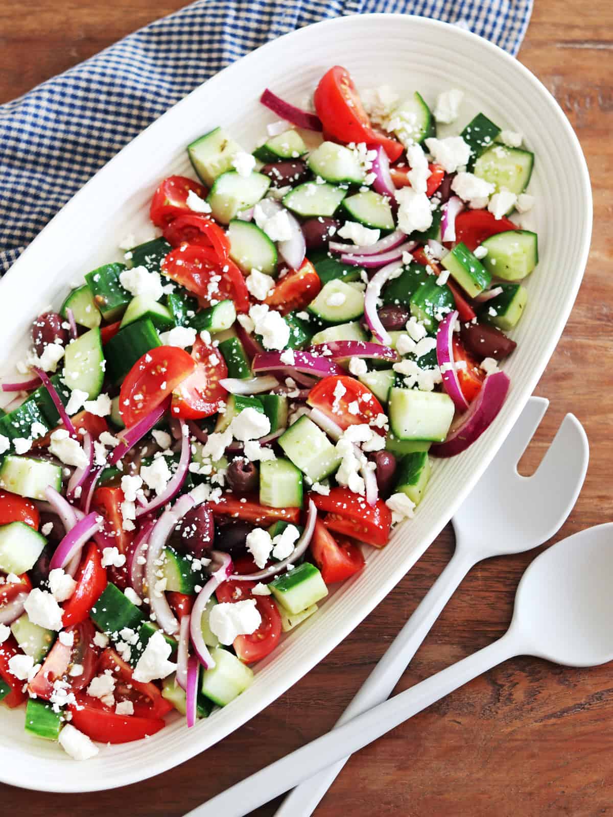 Greek salad in a beige ceramic serving dish on a brown wood table.