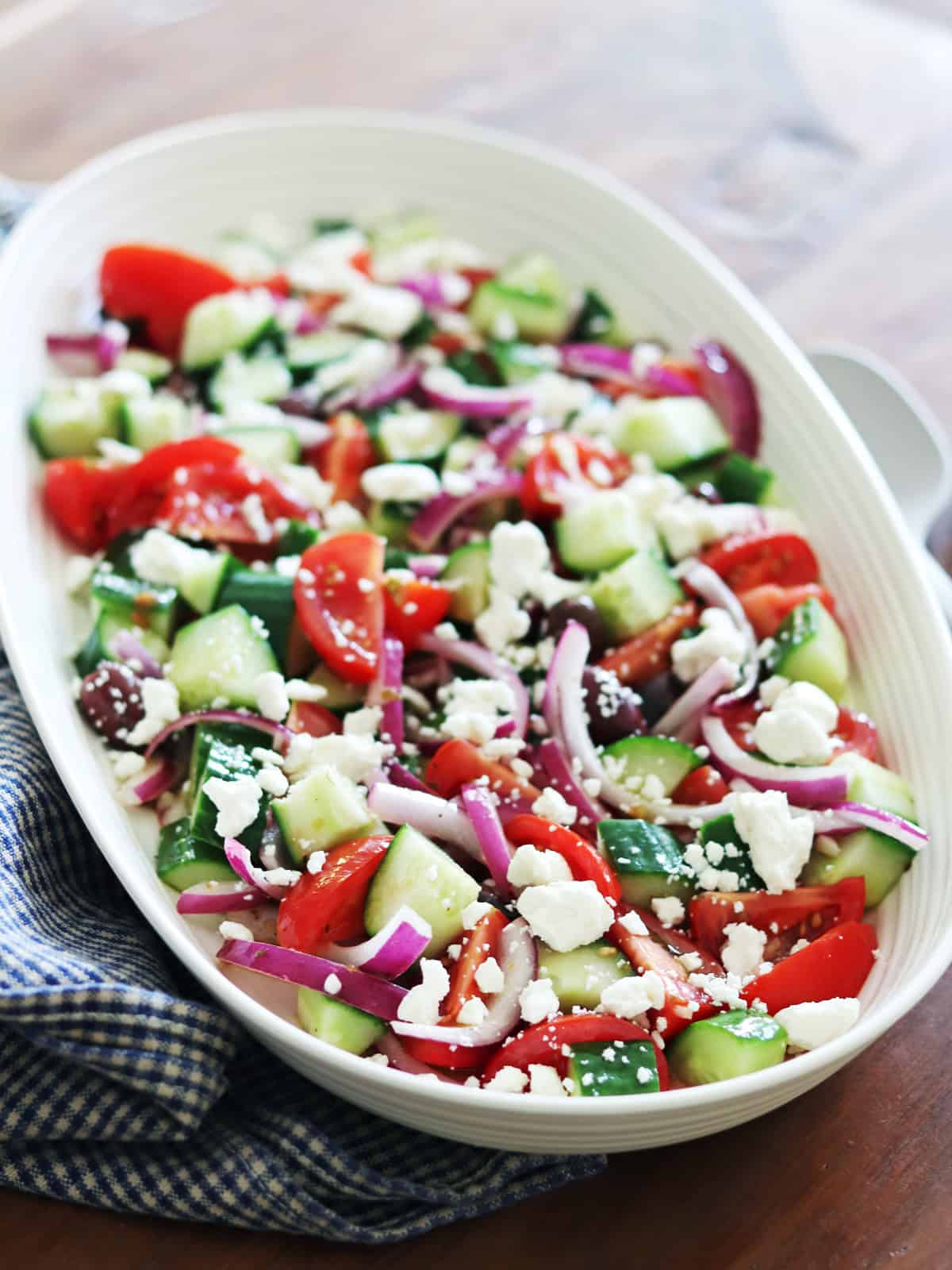 Greek salad on a ceramic beige platter atop a brown wood table.