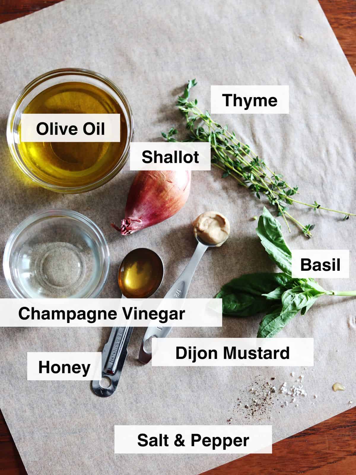 Niçoise salad dressing ingredients arranged on a piece of parchment paper atop a brown wood table.