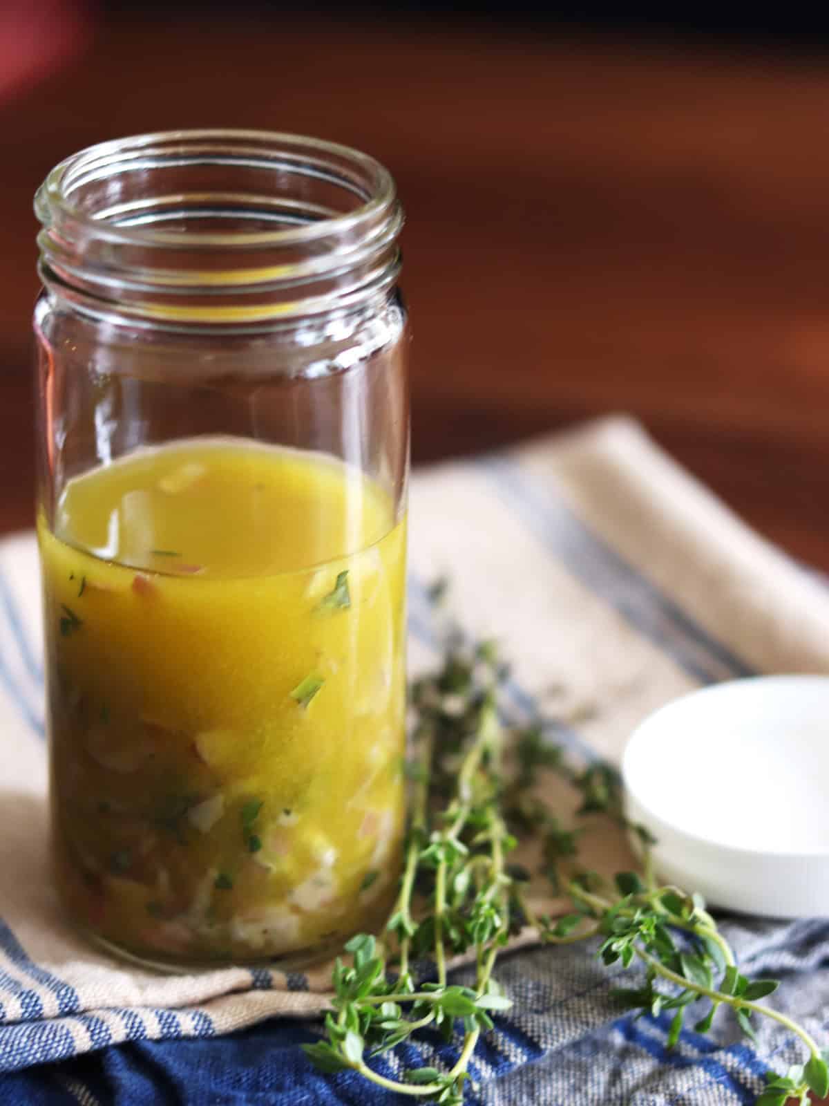 Homemade Niçoise salad dressing in a tall glass jar with fresh thyme alongside it.