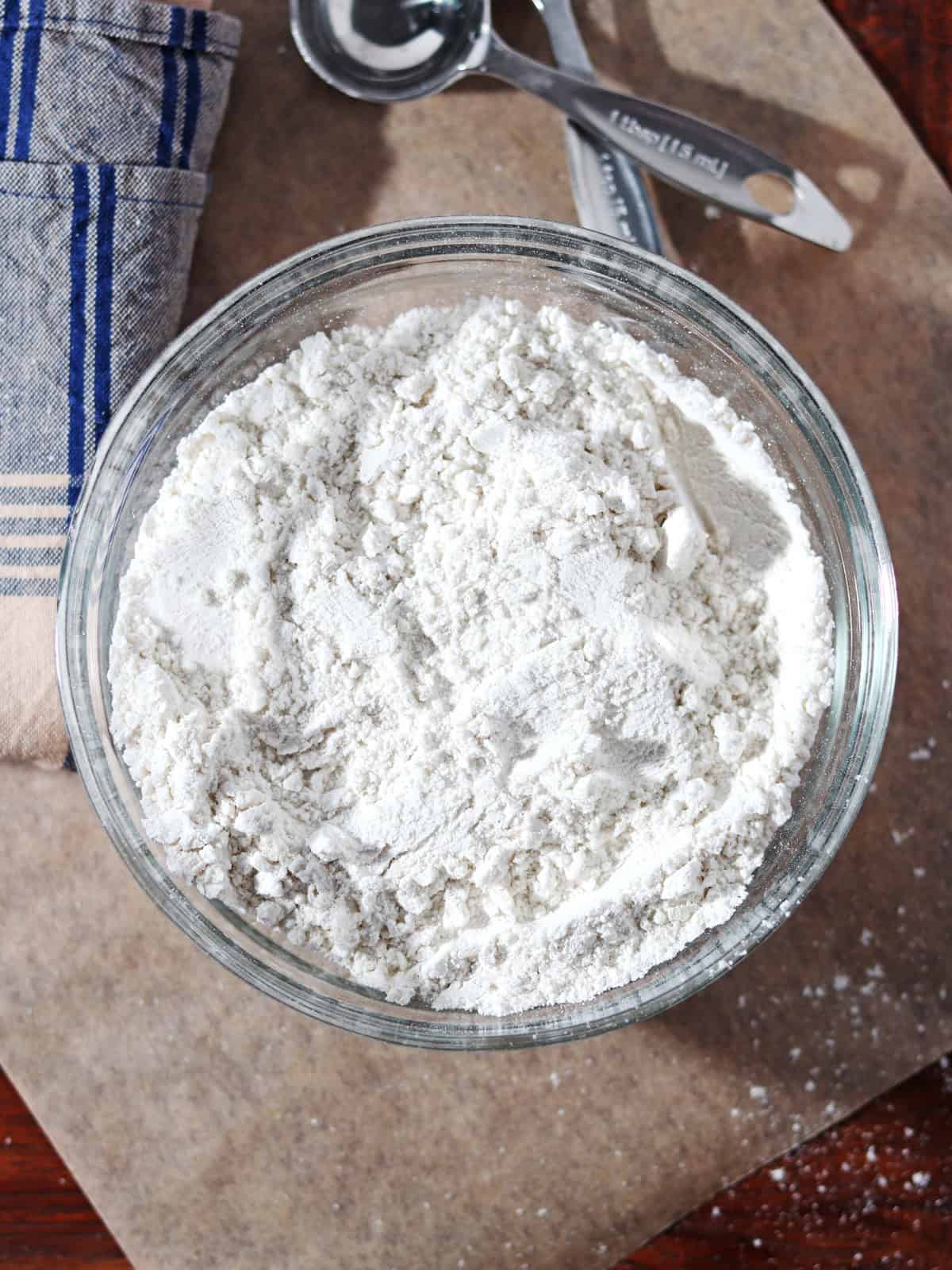 Homemade self rising flour in a glass bowl on a parchment paper lined table.