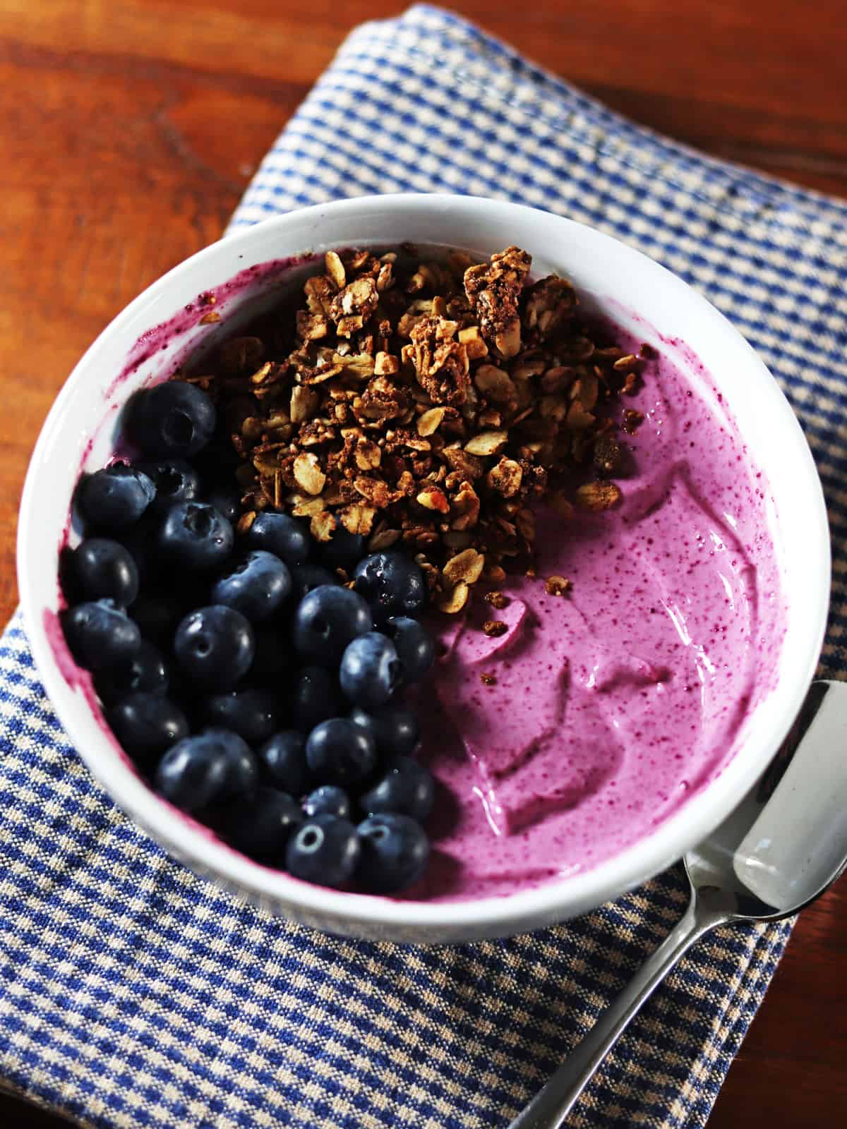 Black raspberry yogurt bowl topped with blueberries and granola on a brown wood table.