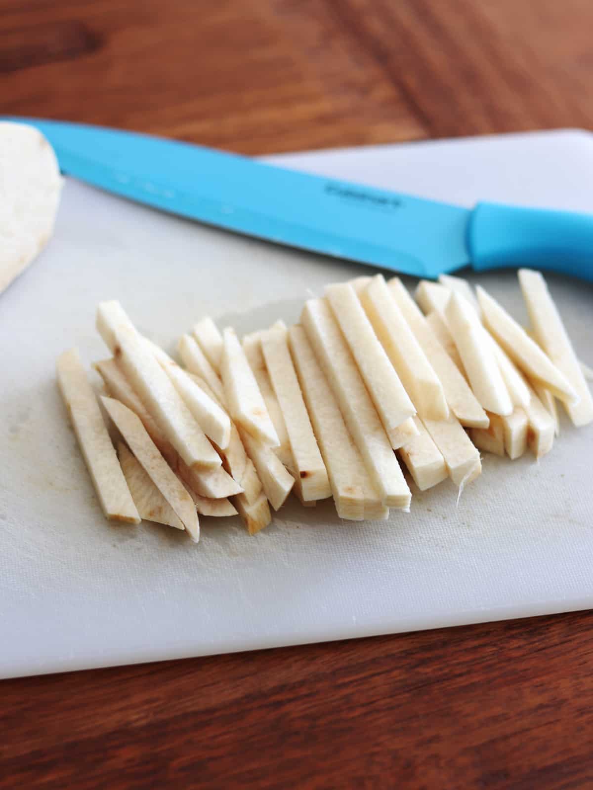 Sliced jicama sticks on a white cutting board.