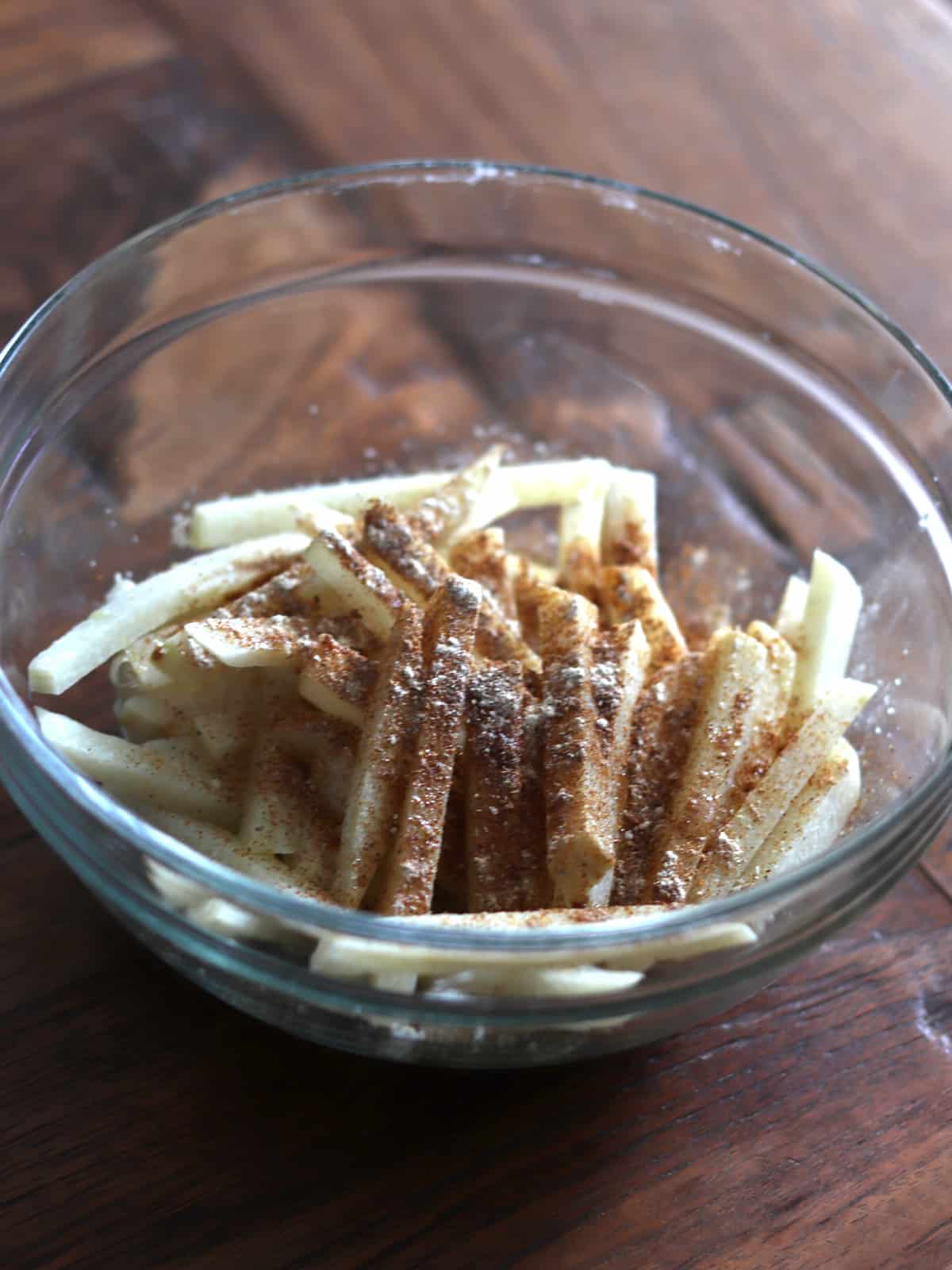 Jicama sticks topped with olive oil and spices in a glass mixing bowl.