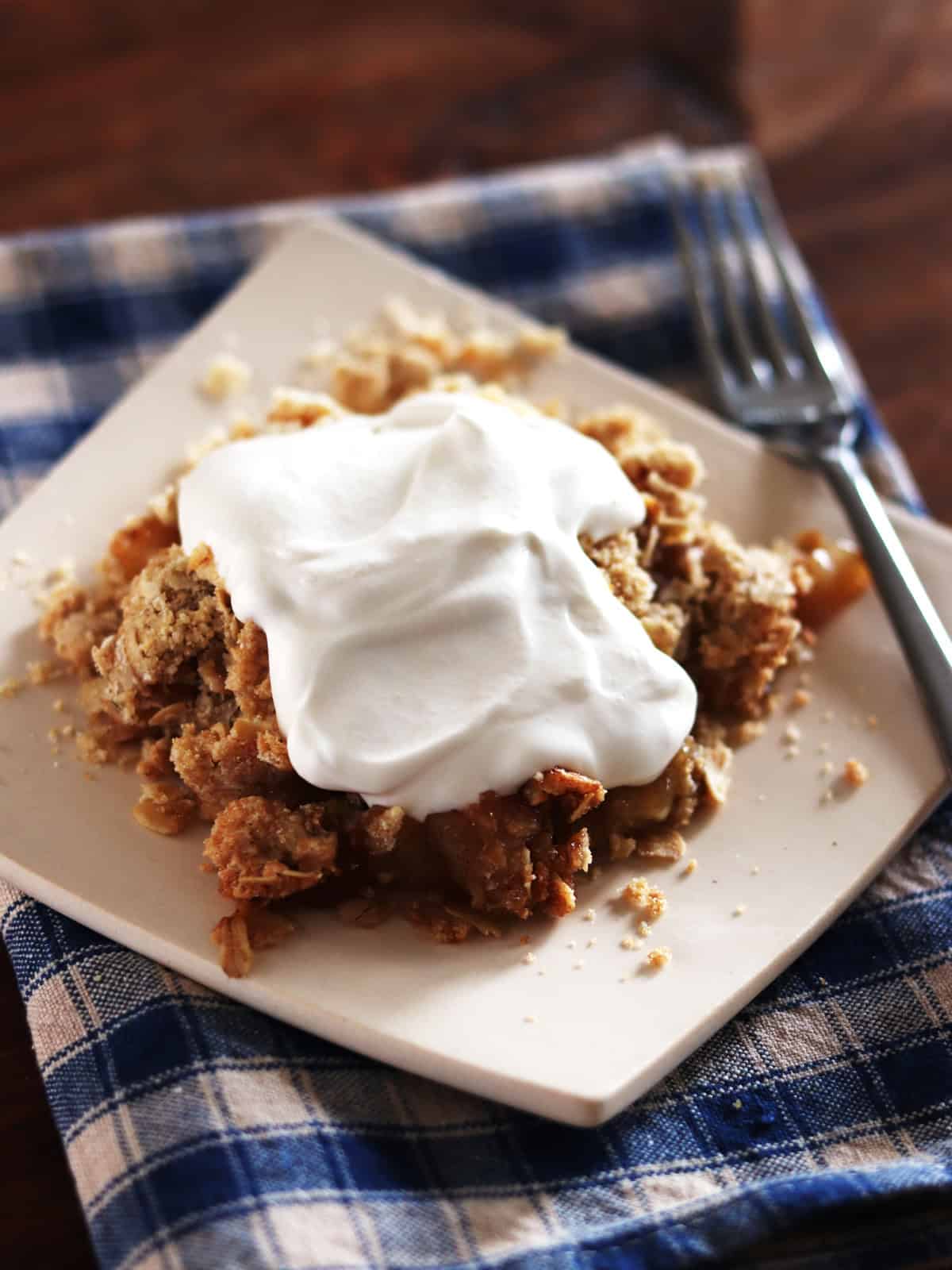 Homemade apple crisp slice topped with whipped yogurt on a brown wood table.