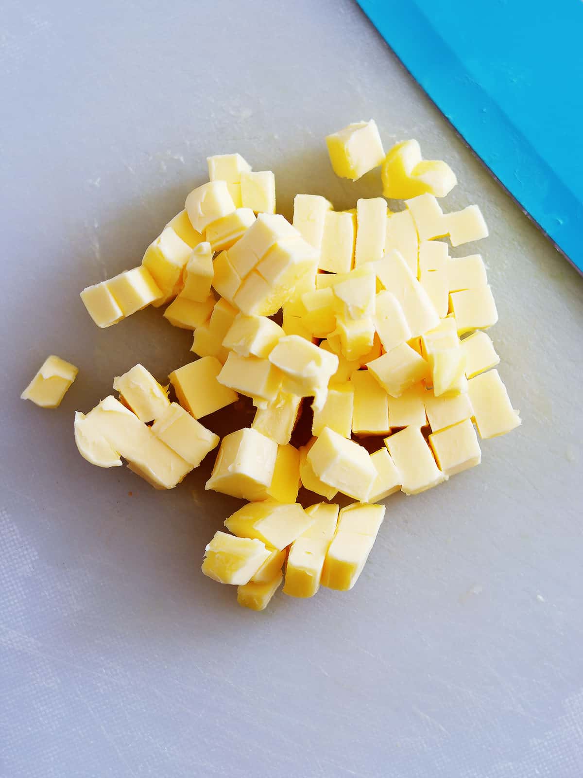Small cubes of butter on a while silicone cutting board with a ceramic blue chef's knife.